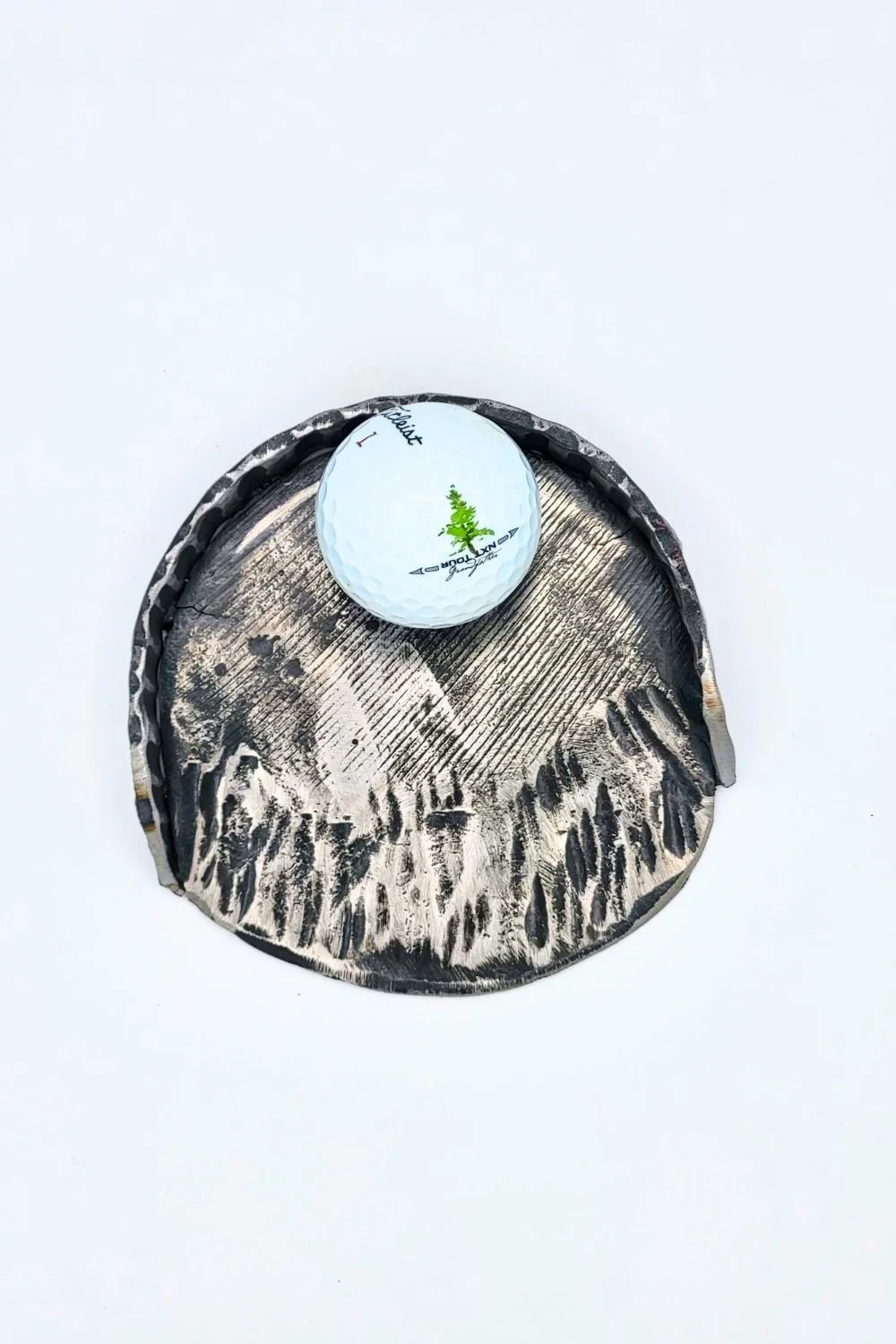 Hand-forged steel putting cup with a golf ball resting inside against a white background.