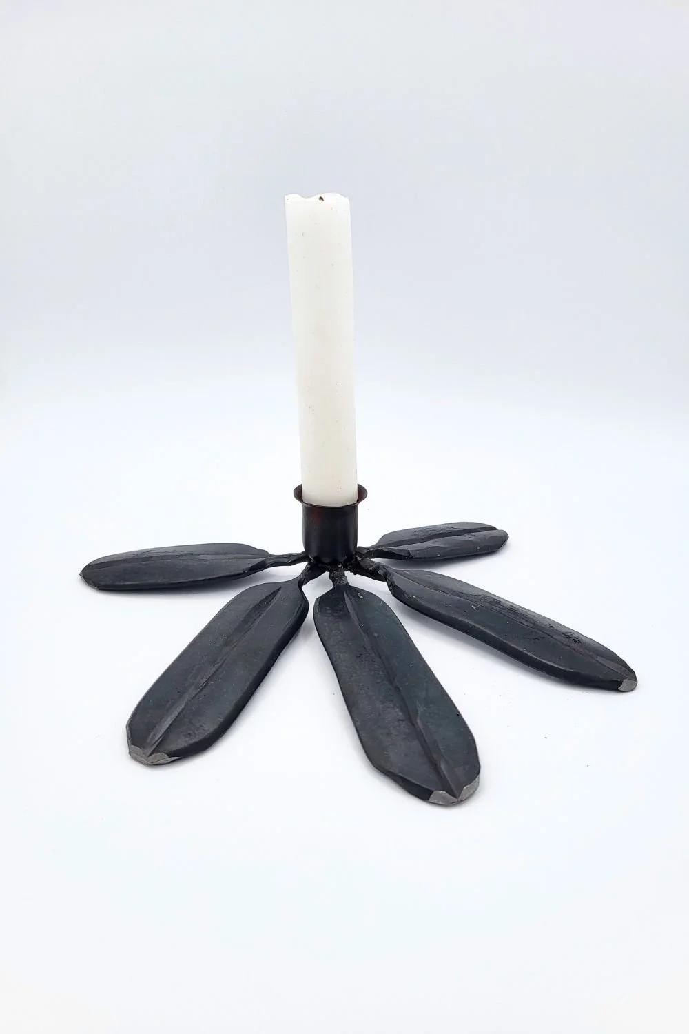 Single blue/grey rhododendron candlestick with taper against a white background.