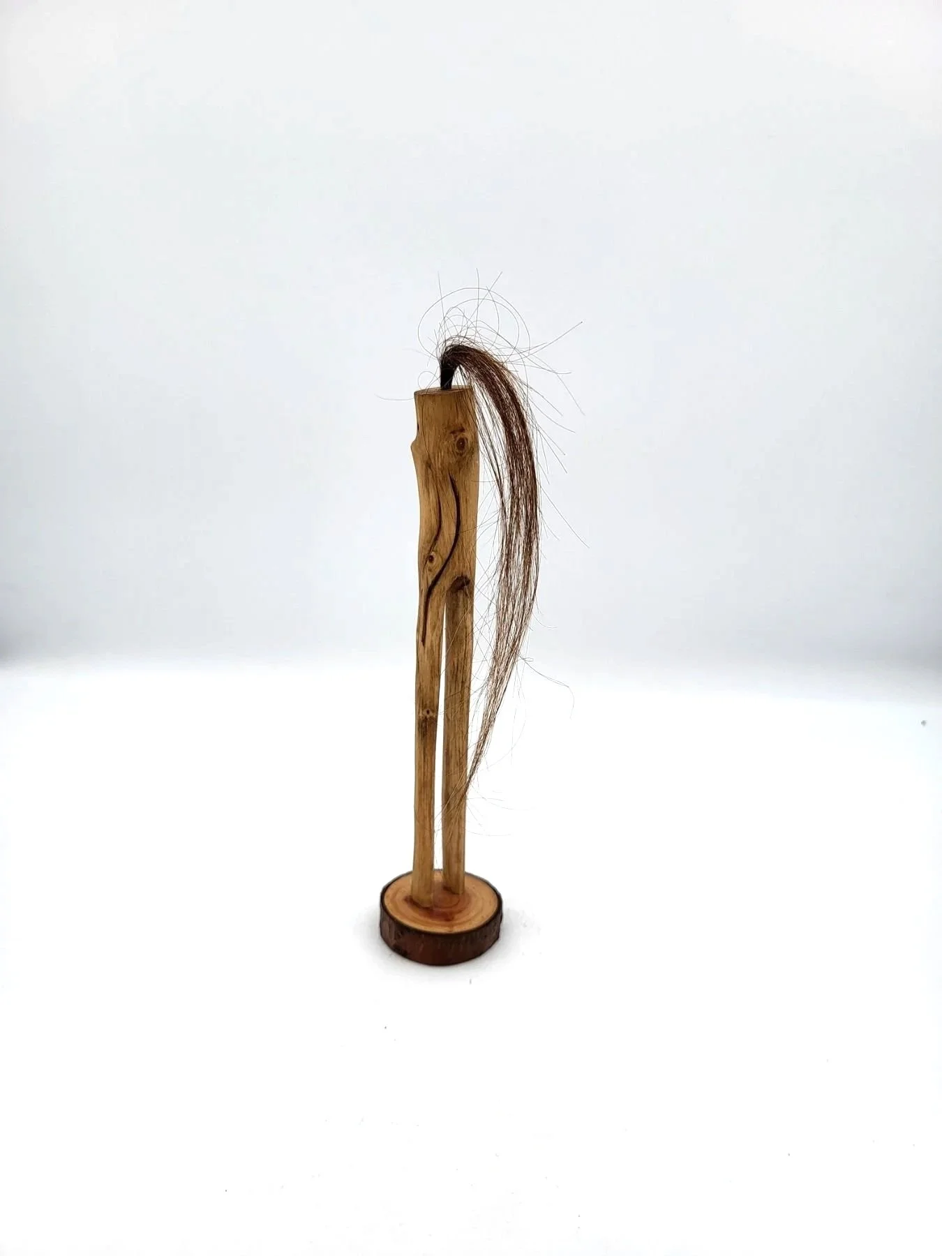 Hand-carved wooden tree creature with long strand of brown hair facing backwards.