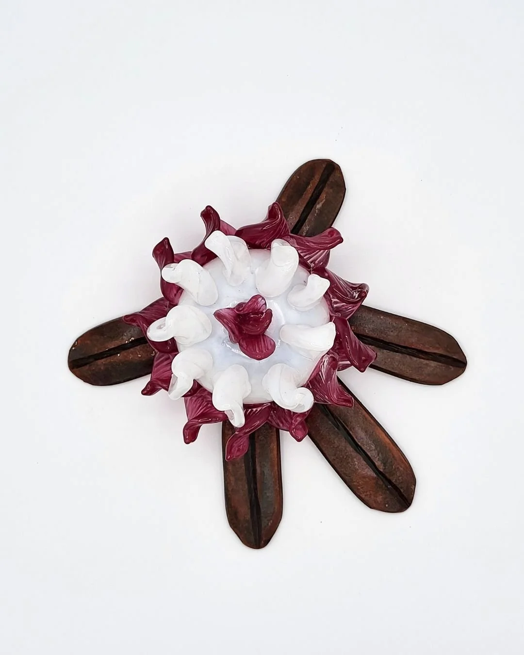 Hand-forged rhododendron leaf with pin and white glass flower nestled in the center against a white background.