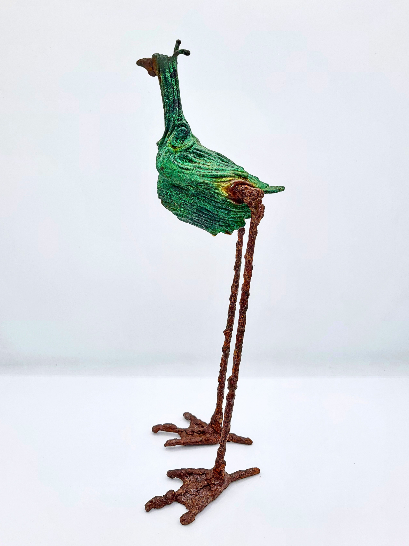 birds sidA long-legged bird statue made from steel with a copper patina faces left against a white gradient background.