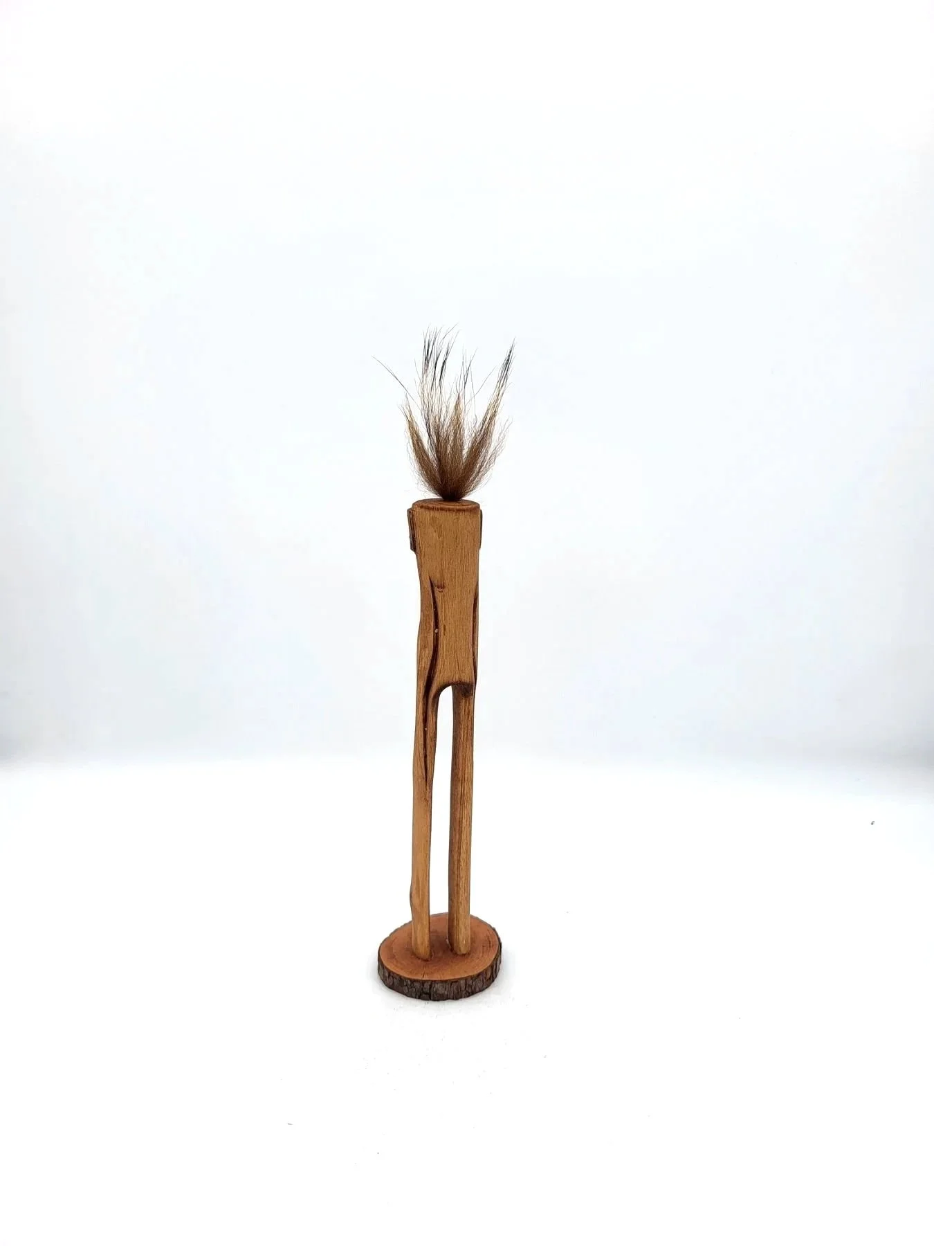 Hand-carved wooden tree creature with tufts of brown hair facing backwards.