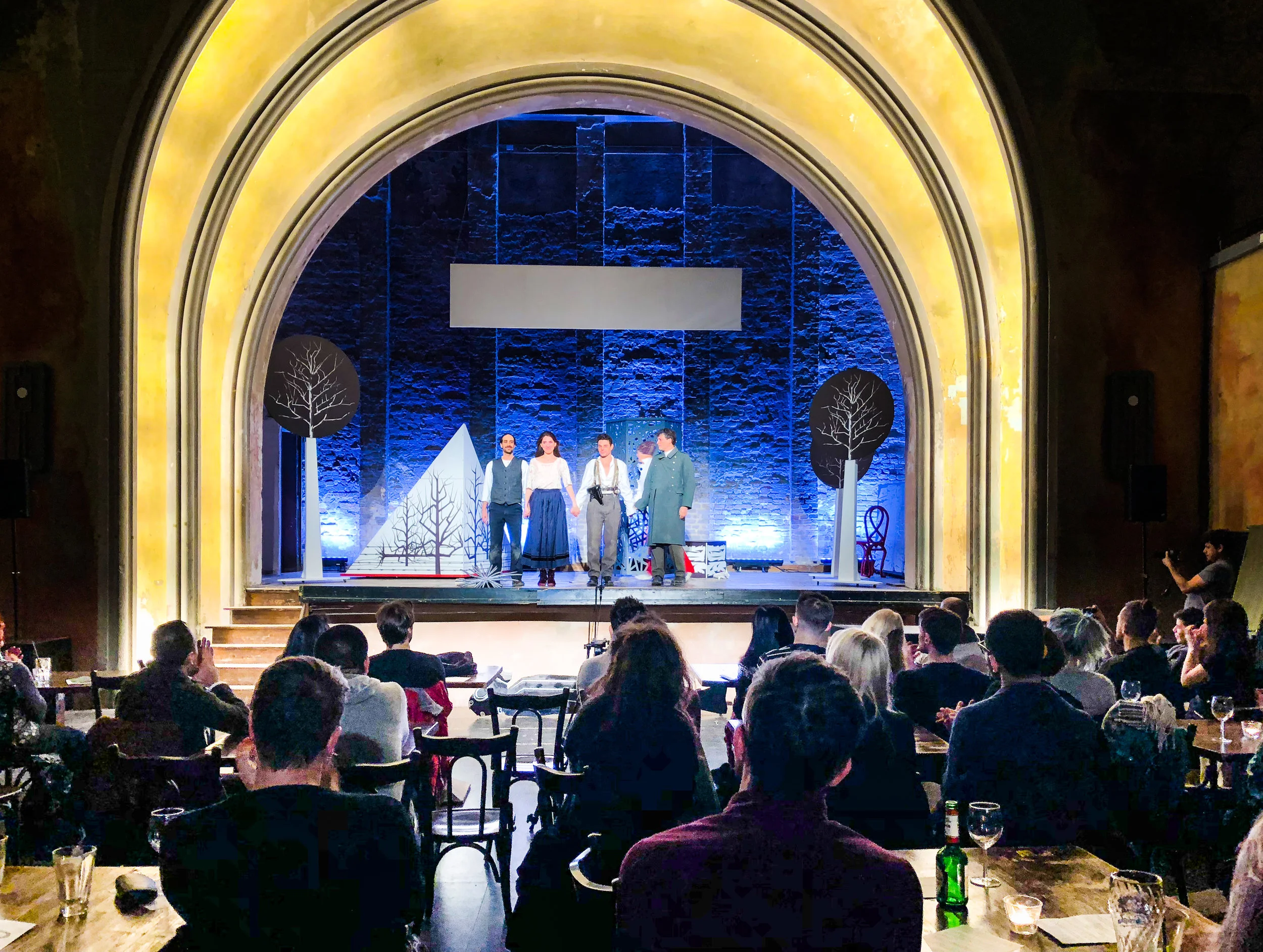The Delphi - old style theatre with bar, people at tables and the performance behind. What a luxurious way to watch a play