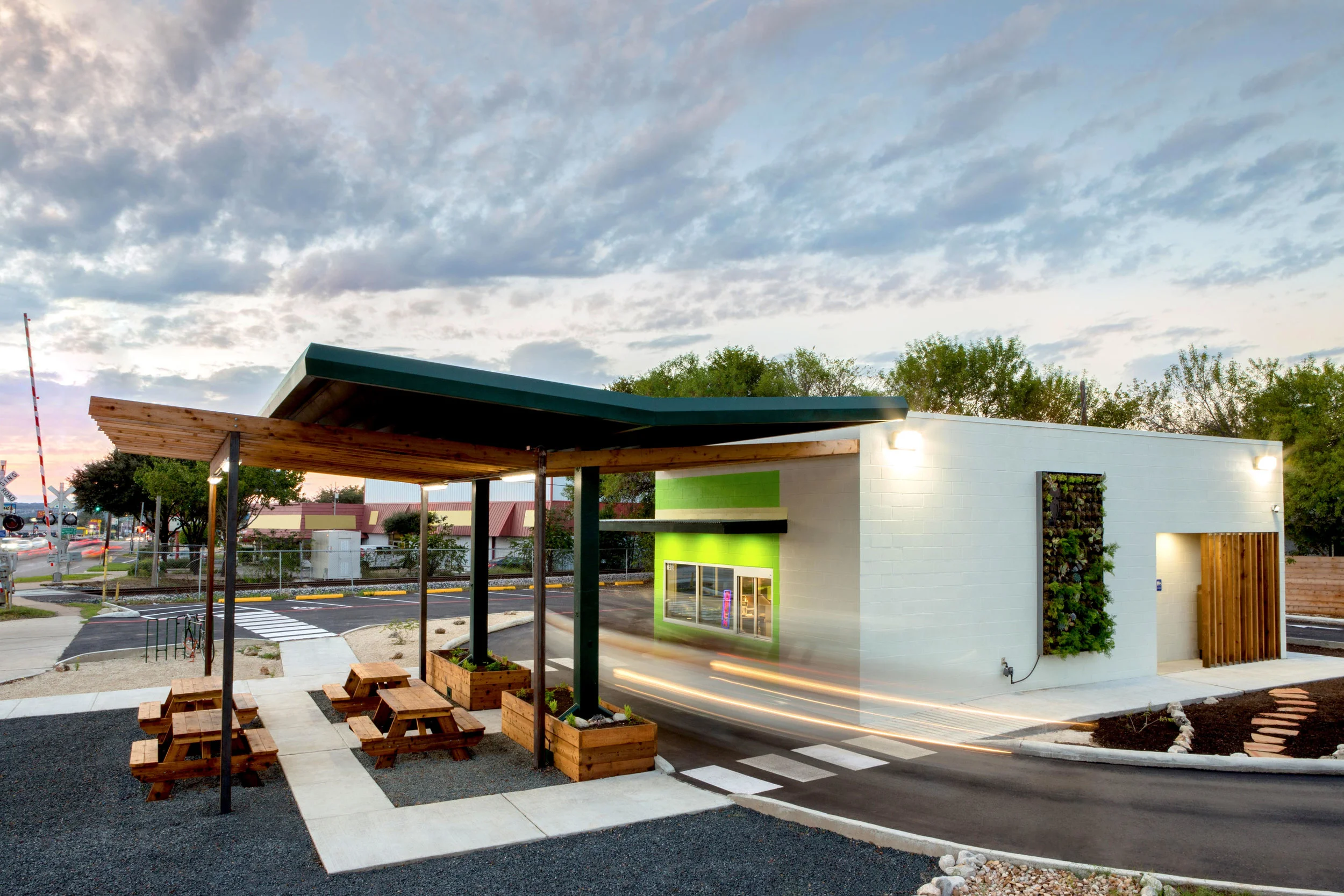 BABY GREENS What was once an auto repair shop overtaken by asphalt, became a drive through salad restaurant and a beautiful landscape. Baby Greens is located in north Austin at a prominent intersection of W.Anderson Lane and Burrell. With the Austin metro rail running on the edge of the site, a green wall, rain water collection, and a restored landscape, sustainability was considered to be a crucial component to the design. The drive-through salad restaurant offering affordable salads also includes a walk-up window, bike racks, and picnic tables where customers can enjoy their food on site. Contractor : Trinity Constructors MEP Engineering : AYS Engineering Structural Engineer : Fort Structures Landscape : Yarrow Landscaping Photo Credits: The Range .