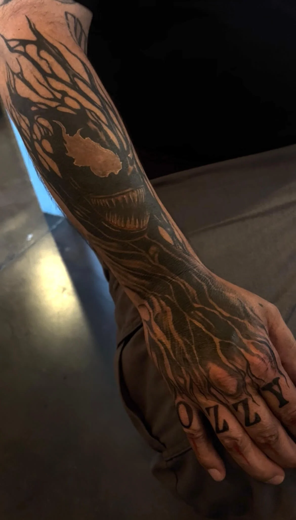 Tattooed arm with a skull and tree design and the word 'NOZUKI' on the fingers.