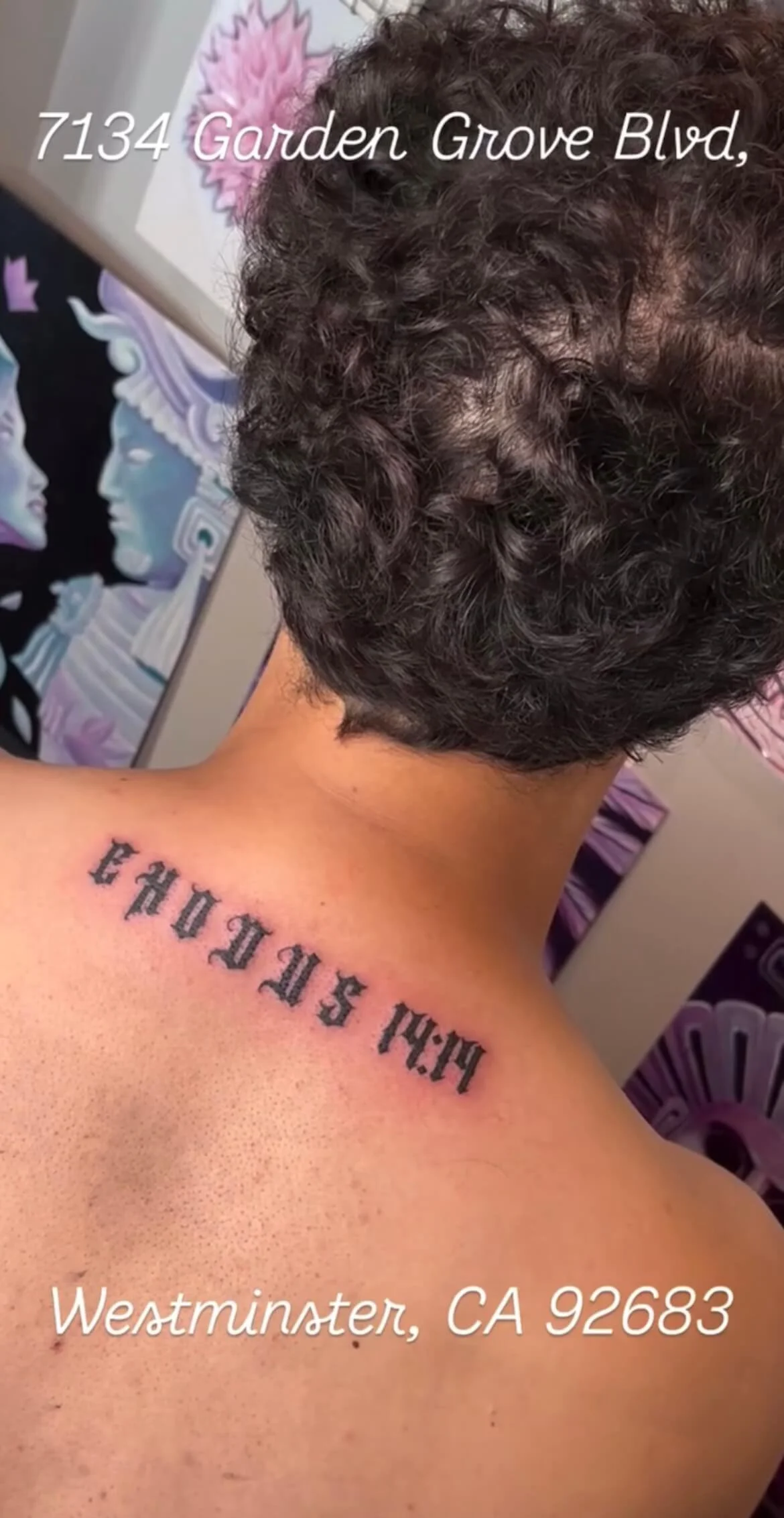 Tattoo on a person's shoulder reading 'HARDCORE' in black gothic font, with background featuring a wall painting of a woman with ocean-themed hair and face.