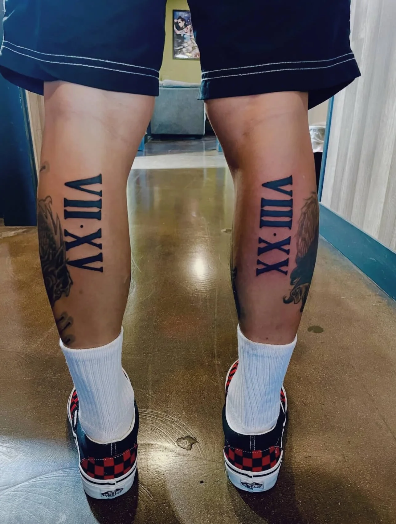 Tattoos on the person's legs with Roman numerals XII.XII.MMXI. These are on both legs, below the knees.