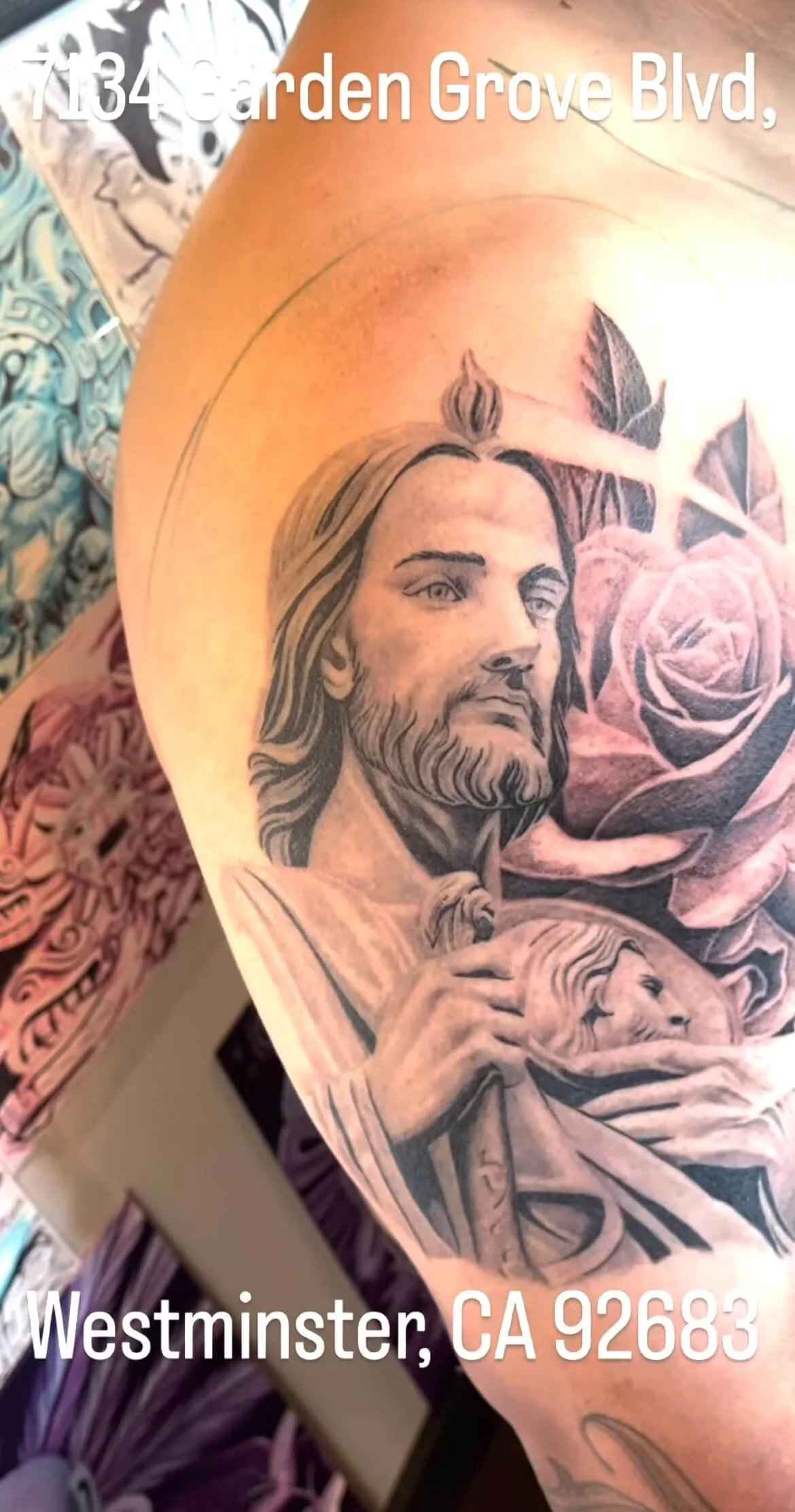 Tattoo of Jesus Christ holding a lion, with roses in the background, on a person's upper arm.