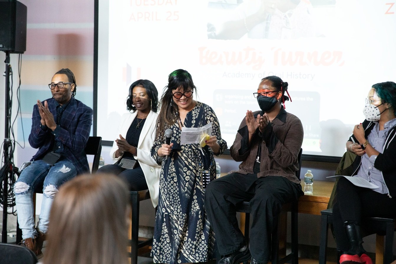  National Public Housing Museum Executive Director Lisa Yun Lee gives opening remarks at the event. Panelist Troy Gaston, panelist Ammie Kae Brooks, panelist and mixtape curator jellystone robinson, and event co-host Eve L. Ewing sit behind her.  