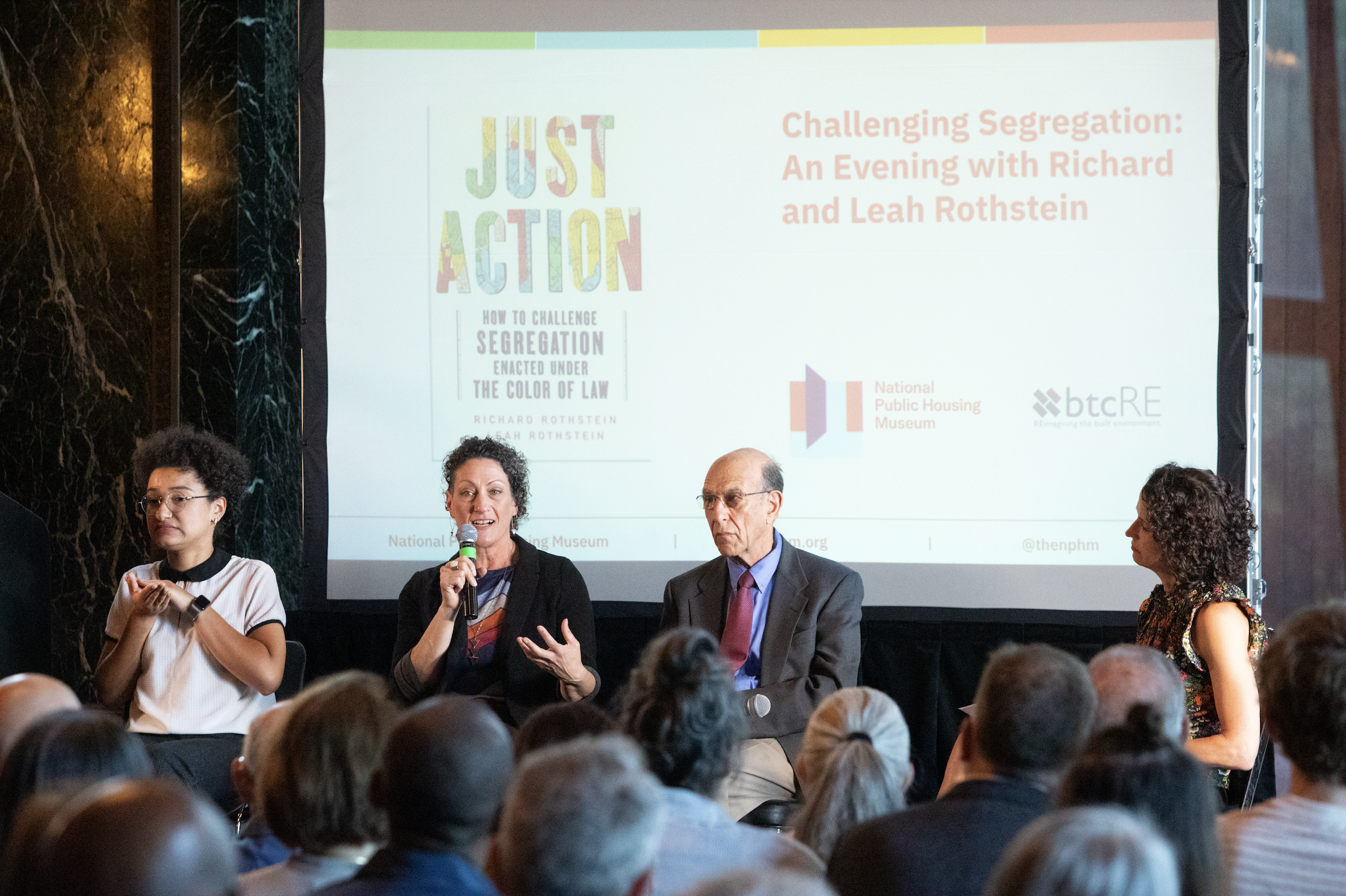  ASL interpreter Makeda Duncan, Leah Rothstein, Richard Rothstein, and Marisa Novara sit in a row in front of a screen. The screen has a photo of the book “Just Action” on it along with logos for the National Public Housing Museum and btcRE.  