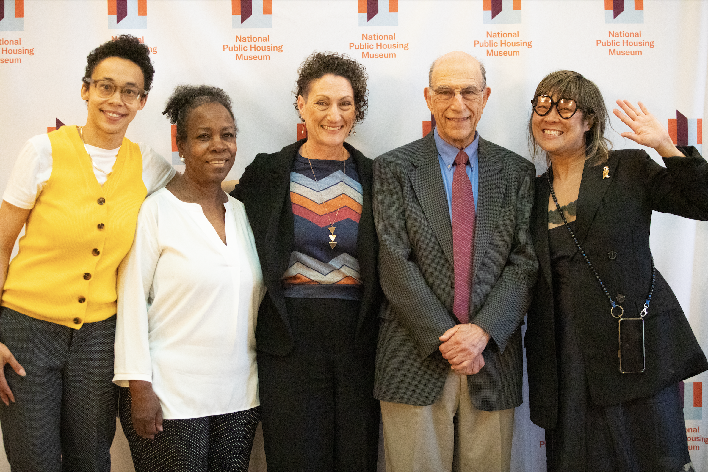  Authors Richard and Leah Rothstein stand with National Public Housing Museum Associate Director Tiff Beatty, Executive Director Lisa Yun Lee, and Board Member Deborah Bennett.  They all stand in front of a branded white banner with small National Pu