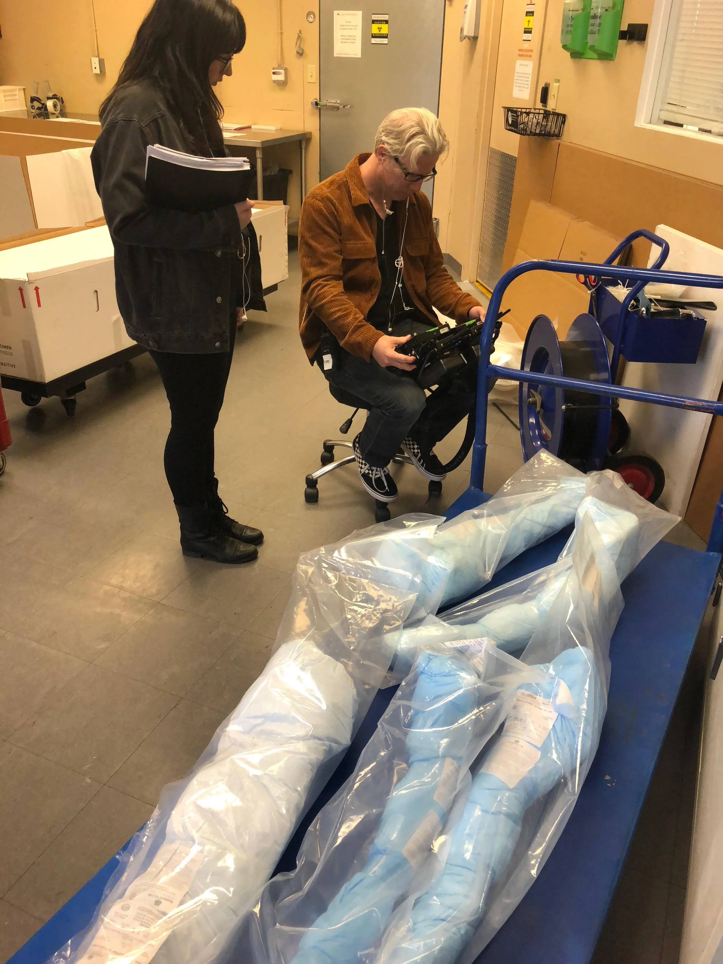 BTS: "In Search Of" with director Eddie Schmidt, checking the monitor next to wrapped spines in a body donation center