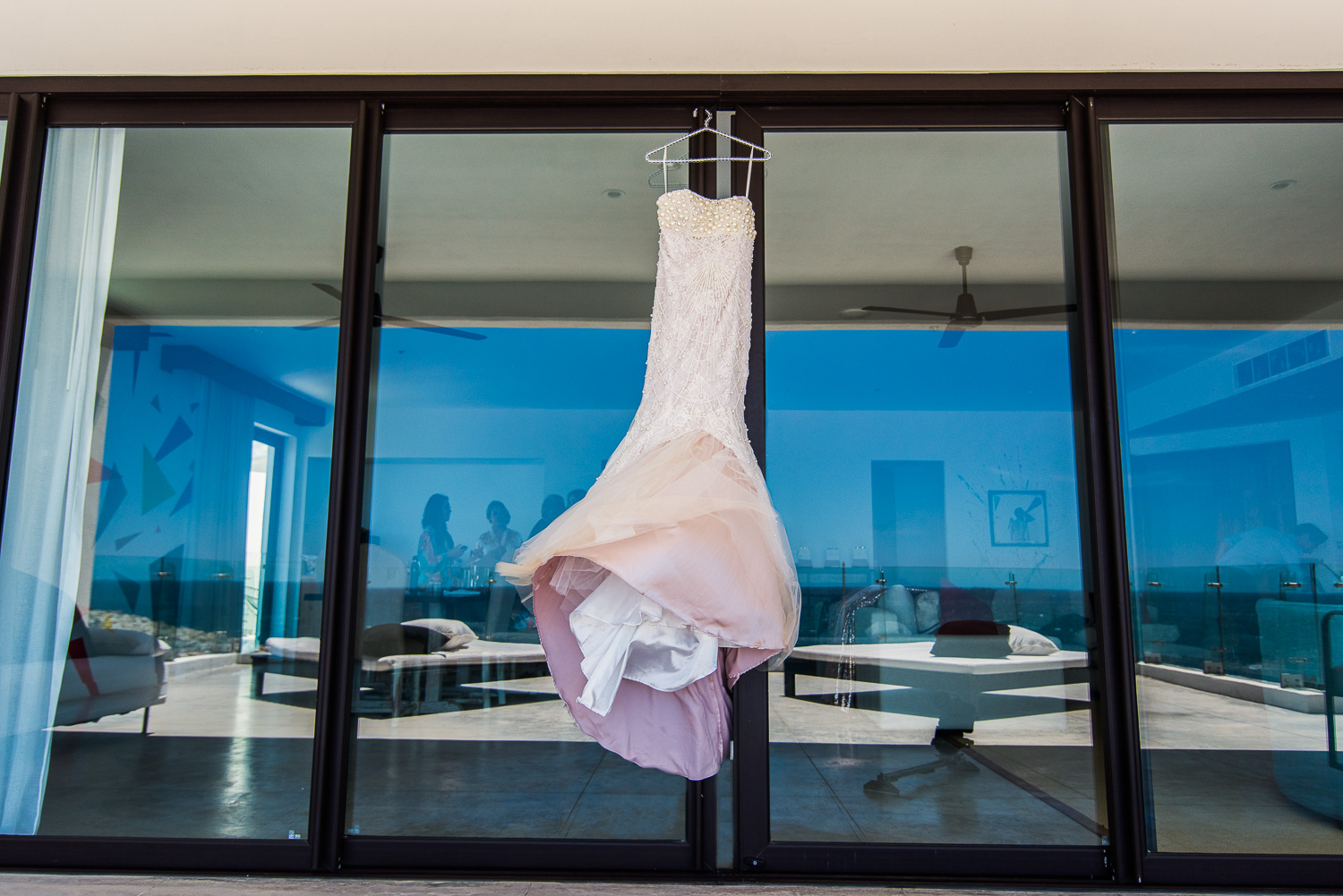  The amazing white gown of the bride is hanging on the window of the room where she is getting ready. On the window you can she the reflection of the blue sky and the ocean. Destination wedding of the wonderful couple Cije and Joseph at the beautiful