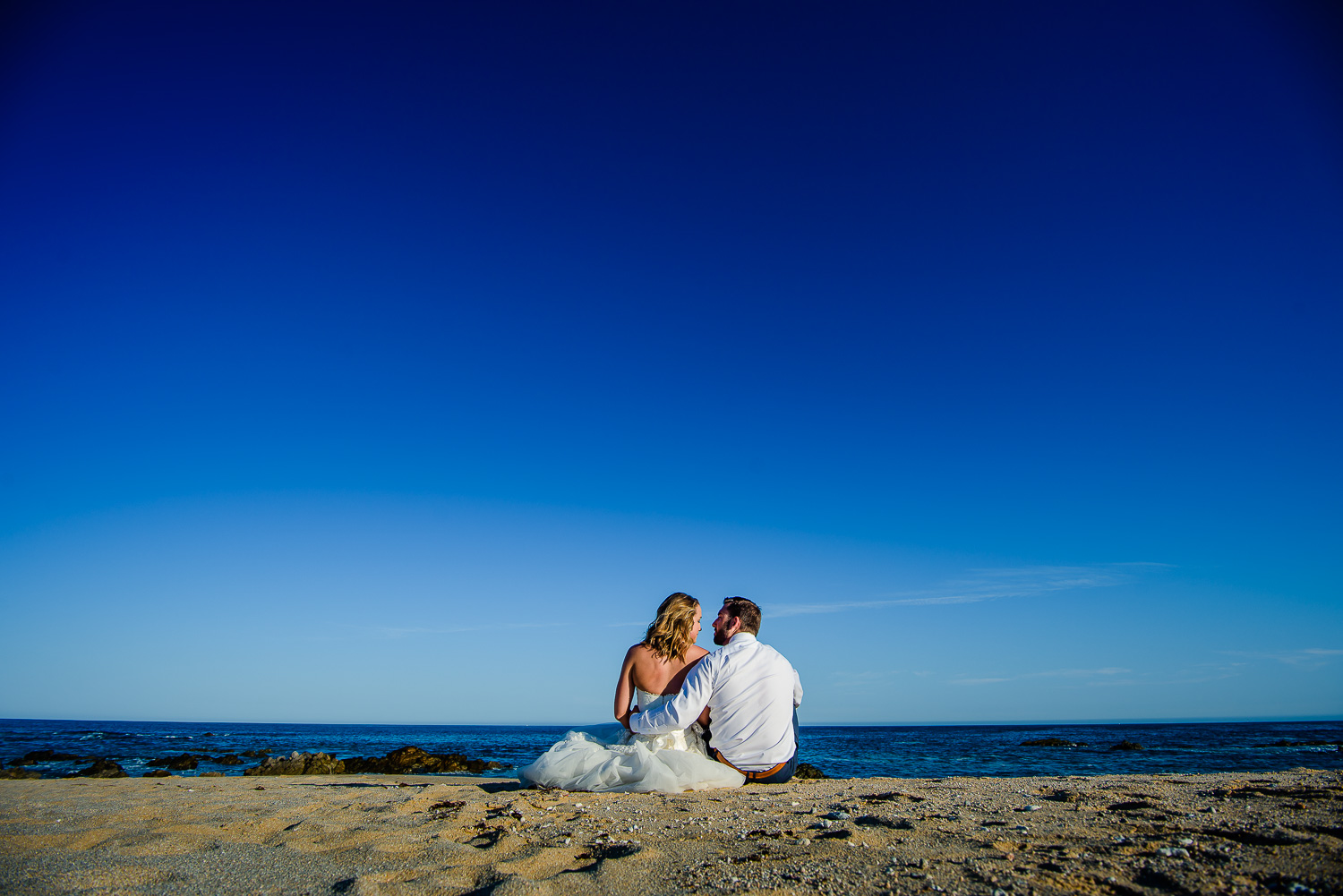  Bride and groom seating on the beach lokking to the Sea of Cortes  