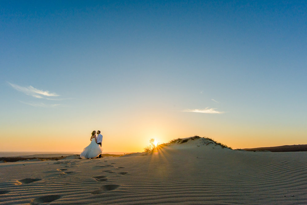 Bride and groom during their sunset photo session on their Cabo wedding. Kissing on the dunes with the sun behind. Photo by talented Cabo wedding photographer GVphotographer https://www.gvphotographer.com/blog/creating-the-perfect-timeline-for-your-…