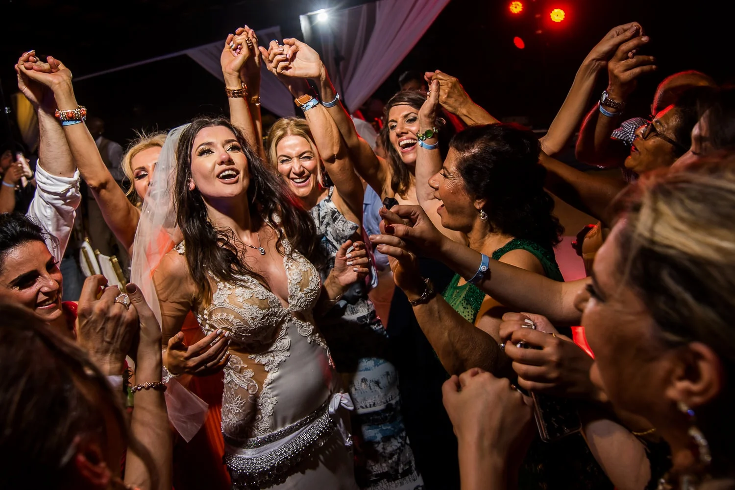 Lovely bride is performing a dance step with the guests at the dance floor The bride is standing with her bridesmaids and friends on the dance floor. They are doing a dance step together on the dance floor. Other guests too are dancing on the beats of music at the evening reception party of the couple- destination wedding of the wonderful couple at the beautiful Acre Baja, Mexico. GVphotographer is an amazing destination wedding photographer based in Cabo San Lucas, Mexico