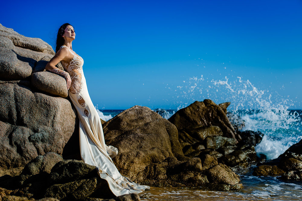 Lovely bride is posing beautifully for the cameraLovely bride is standing on on the rocks and infront of the beautiful blue beach. The bride is looking gorgeous posing for the camera under the bright sun and the rough water - destination wedding of …