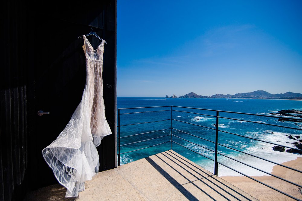 Wedding dress hanging at The Cape with the beach and the Cabo Arch behind