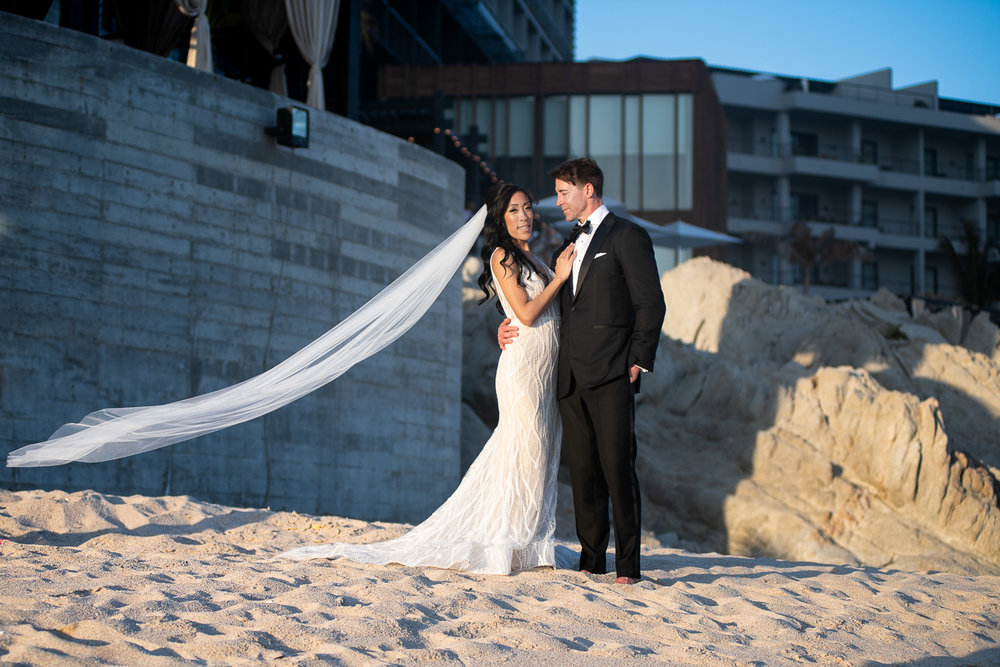 bride and groom posing at the beach with The Cape Resort behind