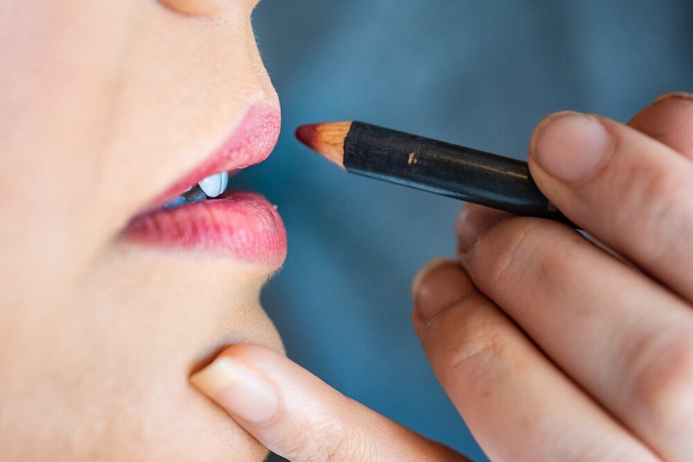 Closeup image of makeup artist painting bride's lips with a red pencil 