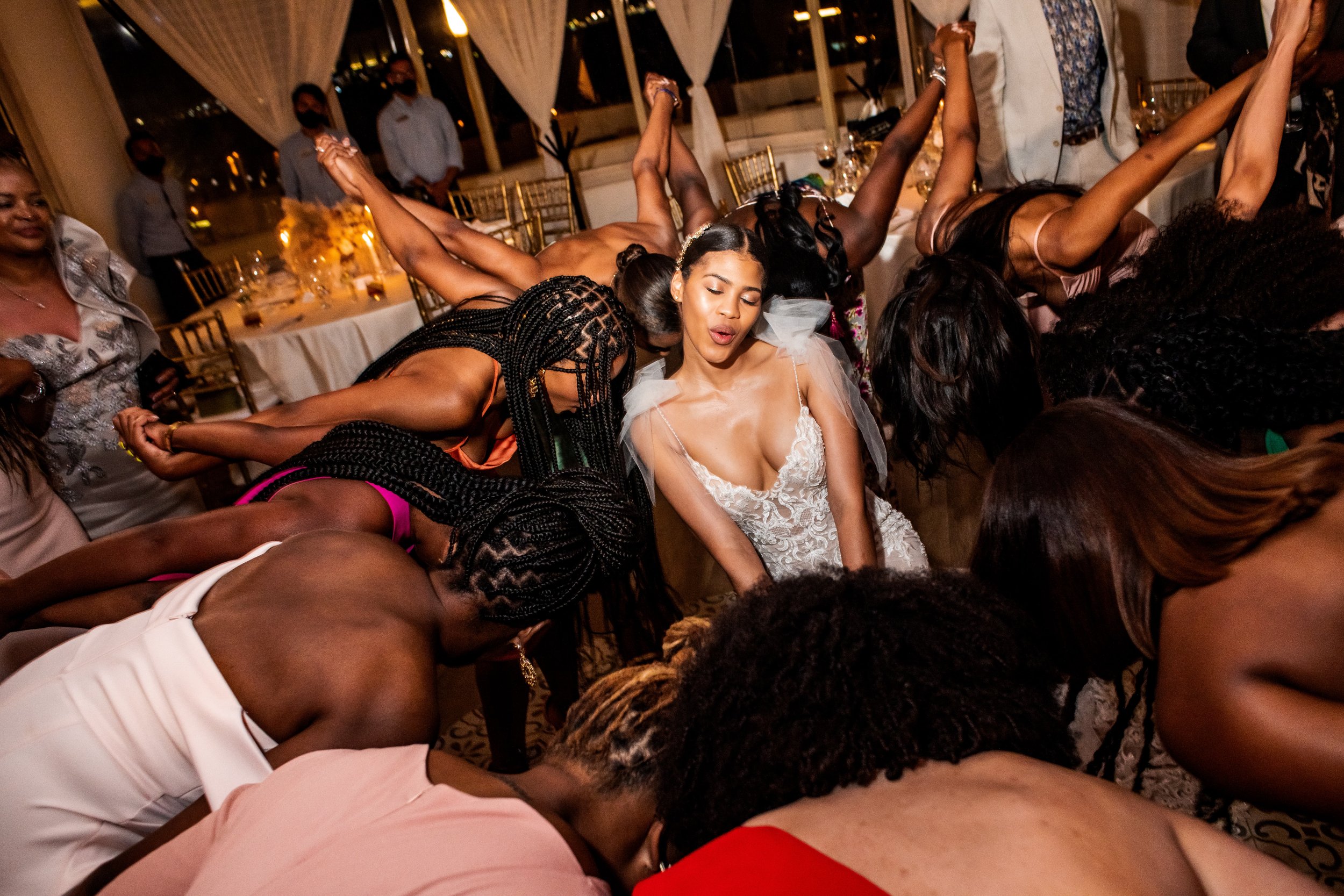 A bride dances joyously surrounded by female guests at a wedding reception, all participating in a lively group dance. the atmosphere is festive and energetic under warm, ambient lighting.