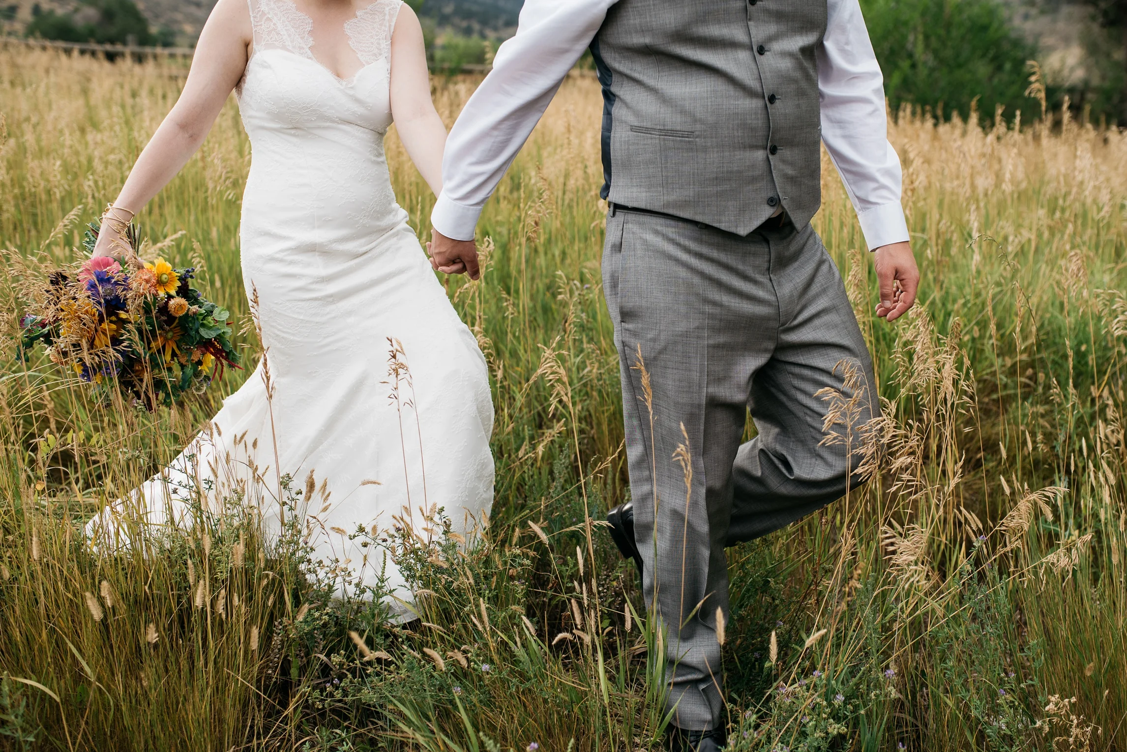 A bride and groom walk though the pastures at Sylvan Dale Guest Ranch on their wedding day. Wedding photography by Sonja Salzburg of Sonja K Photography.&nbsp;