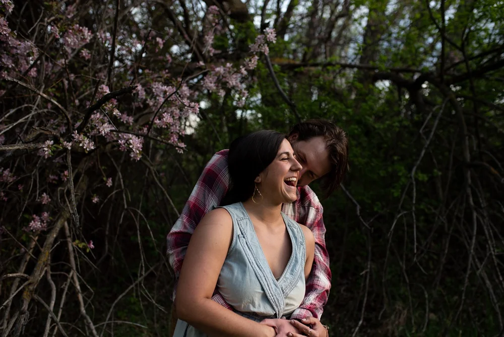 A young engaged couple laughs at an engagement session at Lee Martinez Park in Fort Collins, Colorado. Engagement portrait photography by Sonja Salzburg of Sonja K Photography.&nbsp;