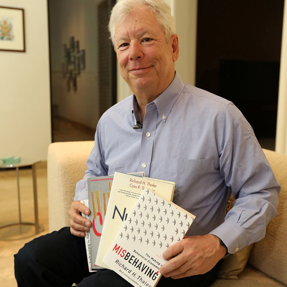 Thaler poses with his books The Winner’s Curse (1993), Nudge (2008), and Misbehaving (2015). Source: The University of Chicago