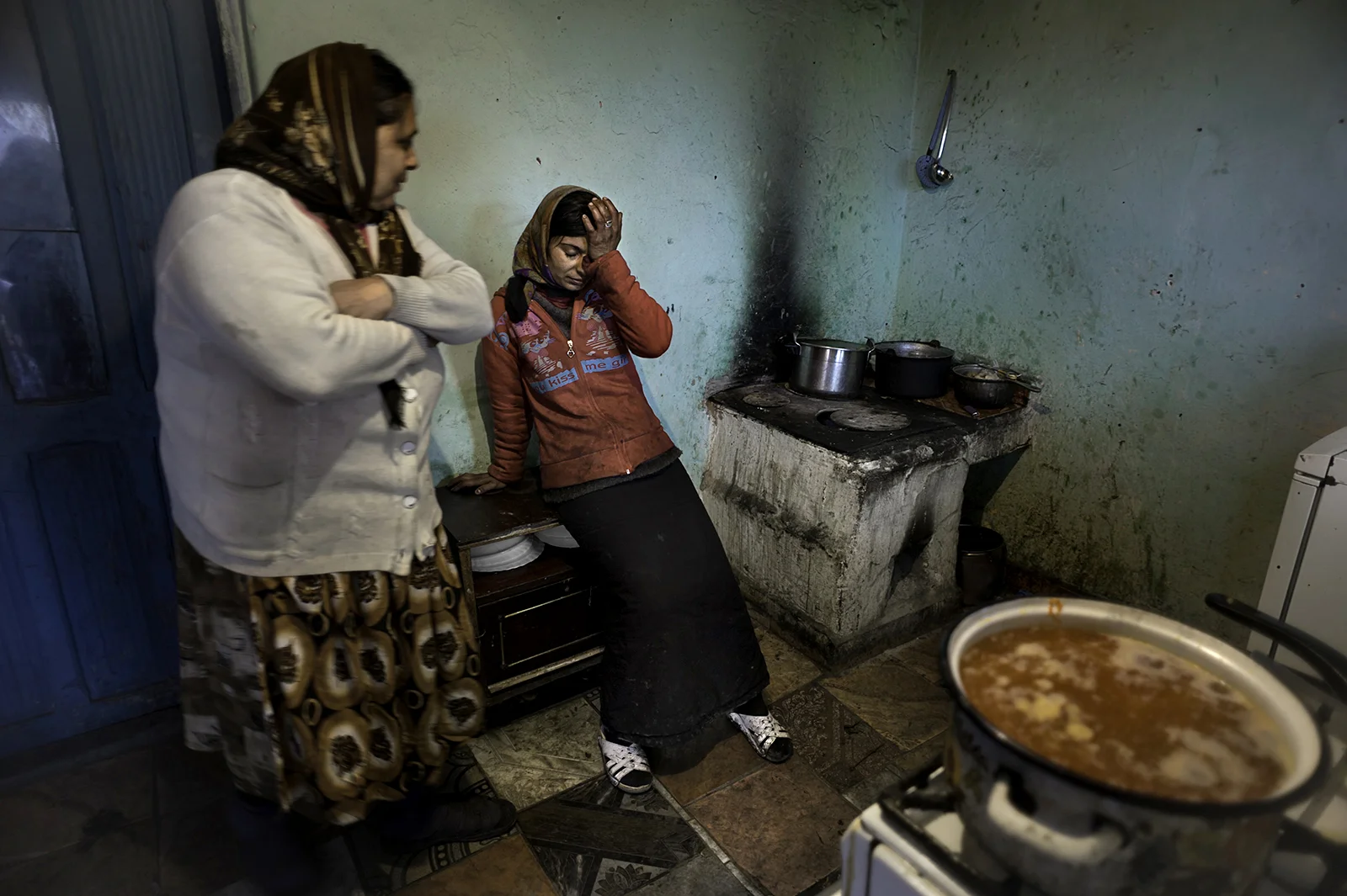Complaining of stomach pains Viorica Gulie, 31, takes a break from cooking soup for her family as her mother-in-law Constanta Gulie, 58, looks on at left. She suffers from Gastritis of her stomach. With no money for medication or to go to the hospital she has to live in pain. Their house which has no running water or a bathroom is built on state land and they don't have title deeds so they are in fear of being evicted. Photo taken in Slatina, Romania.© Renée C. Byer