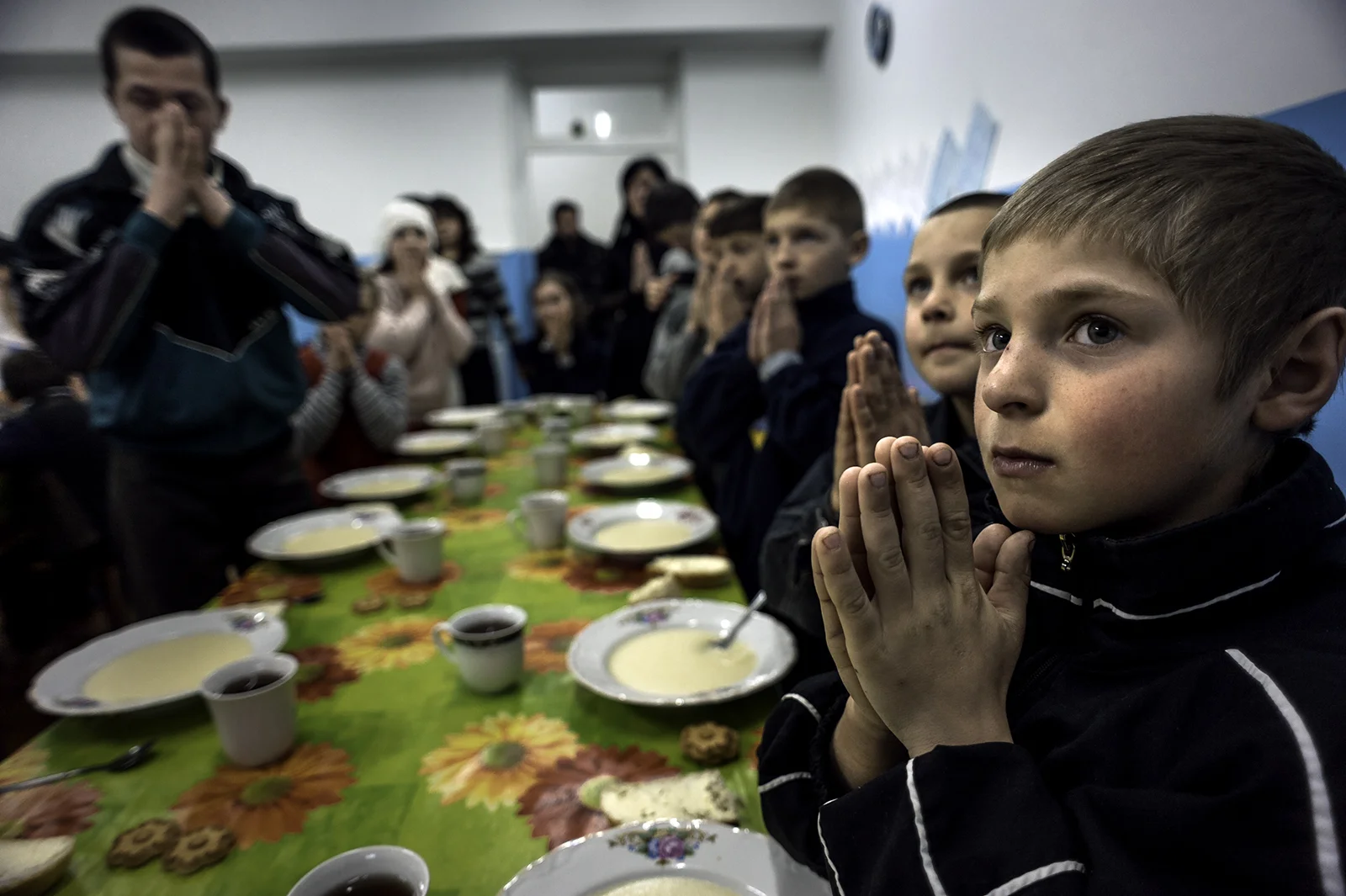 Petru Stepaniuc, 9, right, prays with other children at the Center for Children in Chisinau, Moldova, before a lunch consisting of corn porridge. Petru has lived here since 2009. His father works in Russia but has not sent any money home to help him and his mother, who suffers from alcoholism. This center serves as an orphanage for many children who are left behind when their parents leave the country to try to find work but never return. © Renée C. Byer