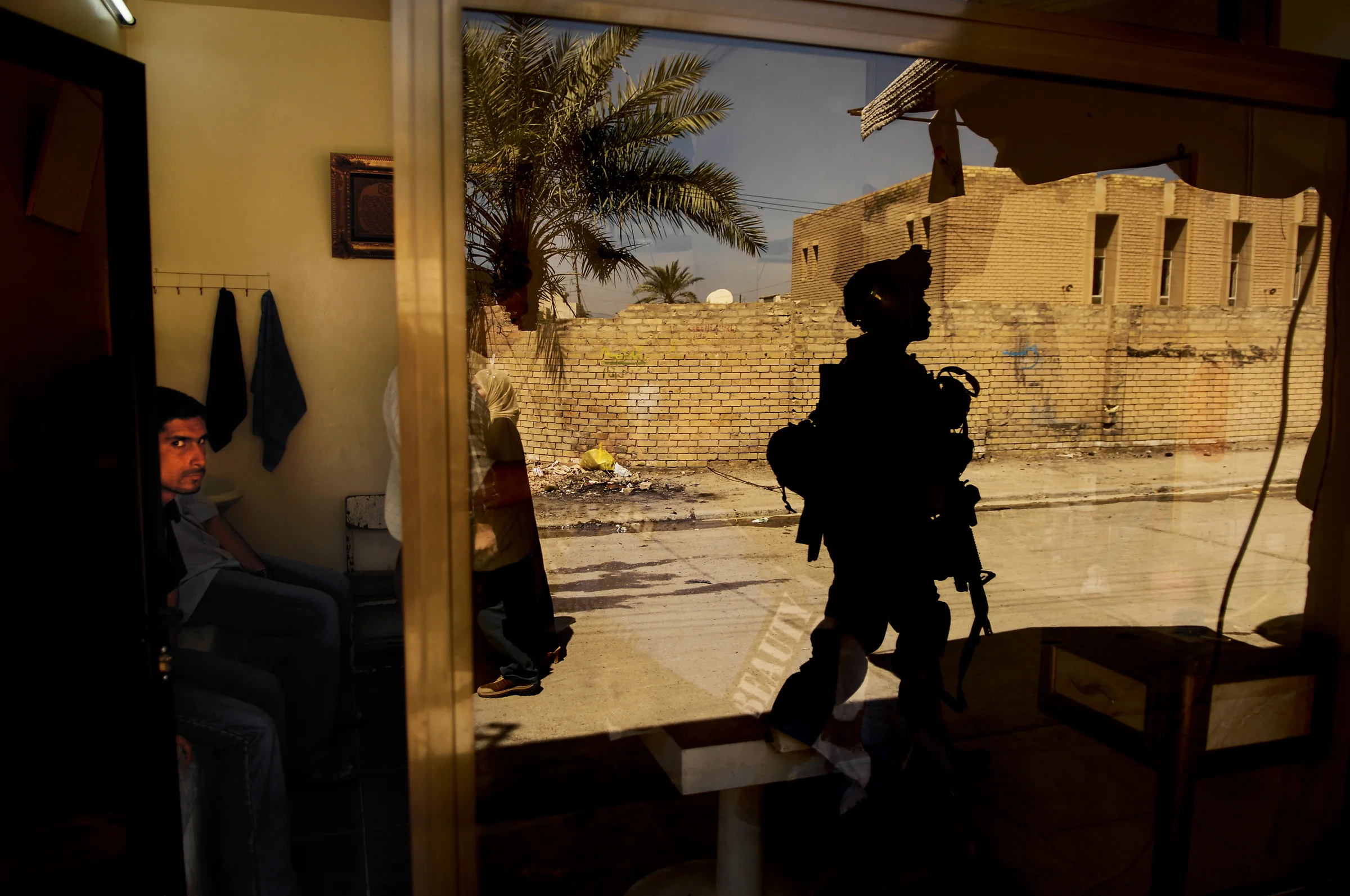 U.S. Army Pvt. 1st Class David Banks is eyed by locals as he walks past a barber shop during a cordon and search in Old Baqubah, Iraq. 2007 © Stacy L. Pearsall