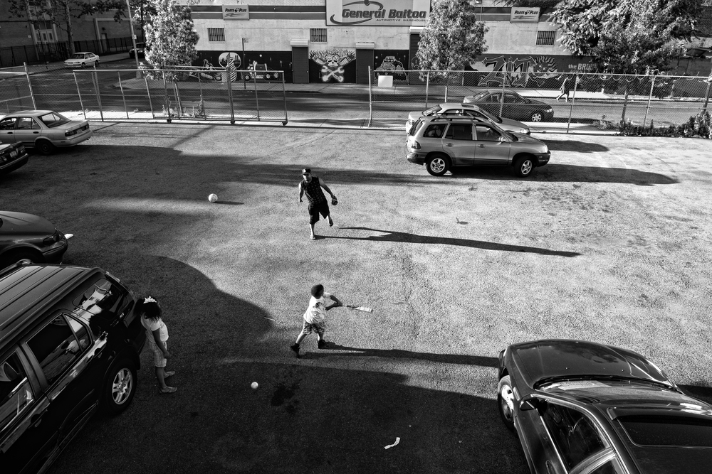  A father uses a parking lot to practice baseball with his son and daughter in the Bronx. 2012&nbsp;© Zun Lee 