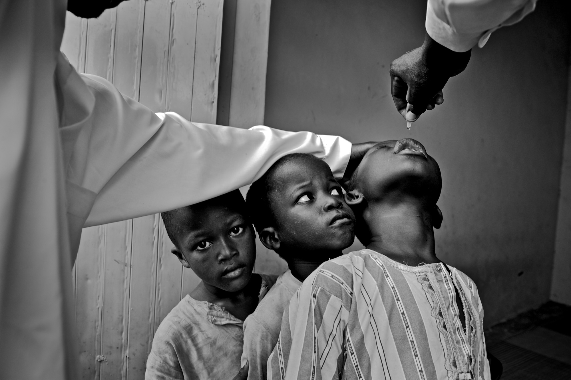 Nigeria's Polio Nightmare: Kano, Nigeria - Boys wait their turn for vaccinator Sani Mohammed to administer two drops of polio vaccine on their tongues at a stationary vaccine site. © Mary F. Calvert/The Washington Times/ ZUMAPRESS.com
