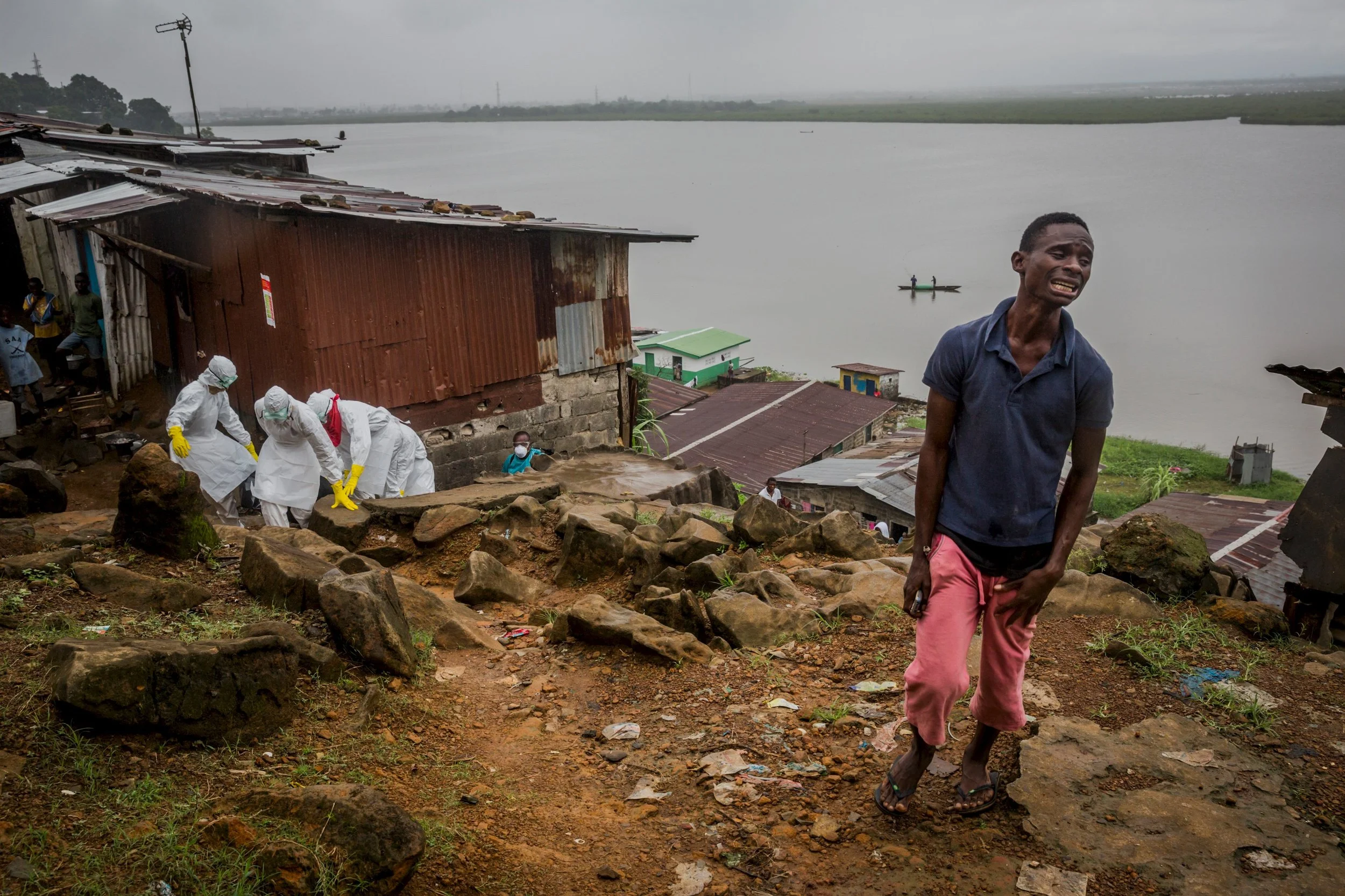 Eric Gweah, 25, grieves as he watches members of a Red Cross burial team carry the body of his father, Ofori Gweah, 62, a suspected Ebola victim, in a riverside area called Rock Spring Valley in central Monrovia, Liberia. September 18, 2014 © Daniel Berehulak for The New York Times