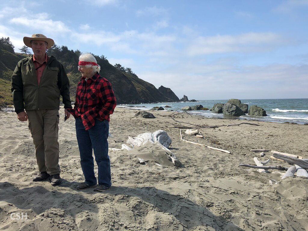  Frank and Cheryl chat in front of the black sandstone outcrop in the surf at the beach. 