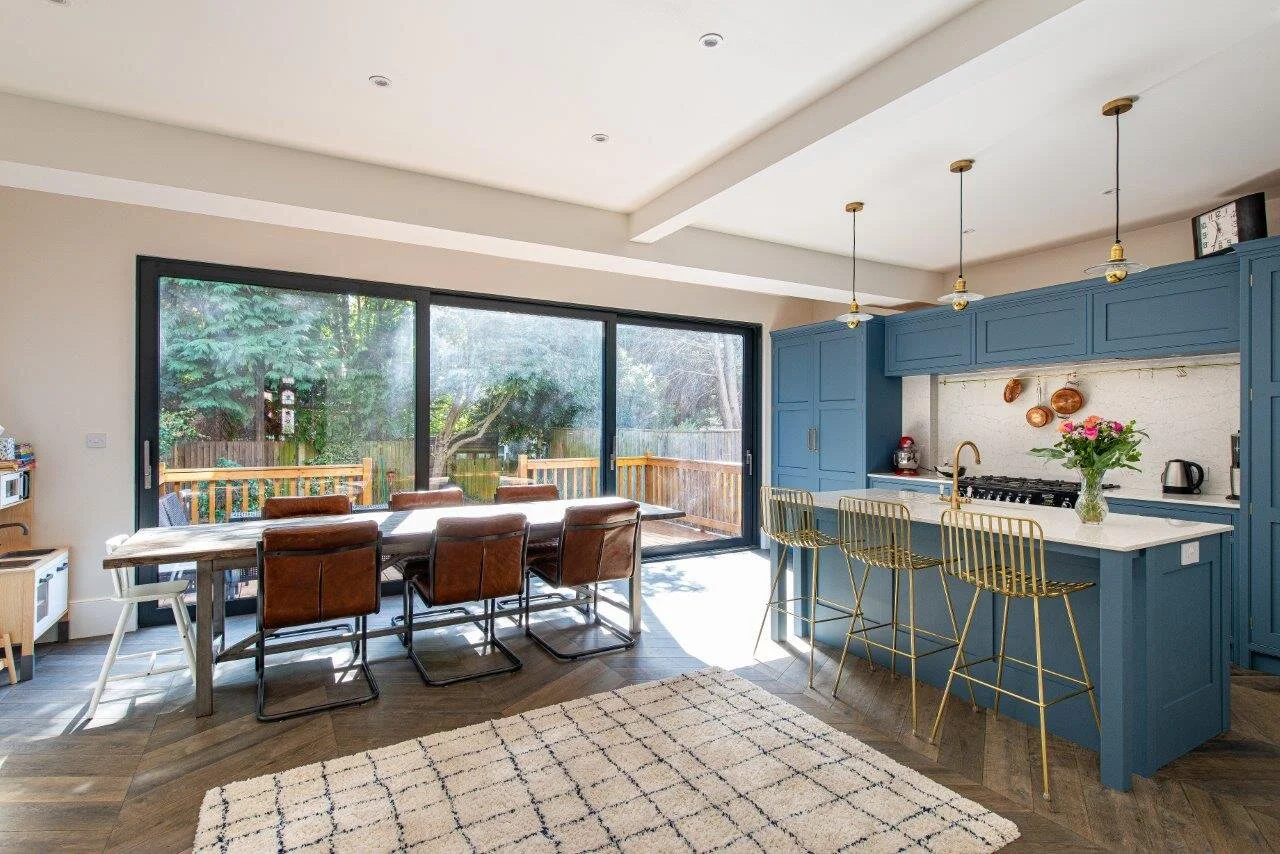 Open plan kitchen and dining room with blue cabinetry and white quartz worktops and splashback.
