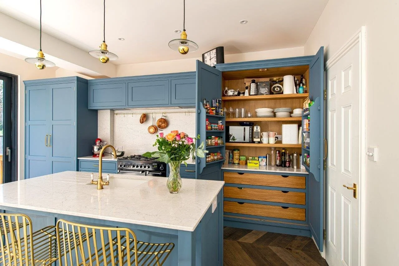 Blue kitchen with quartz worktop and brass handles & tap with large double doored pantry.