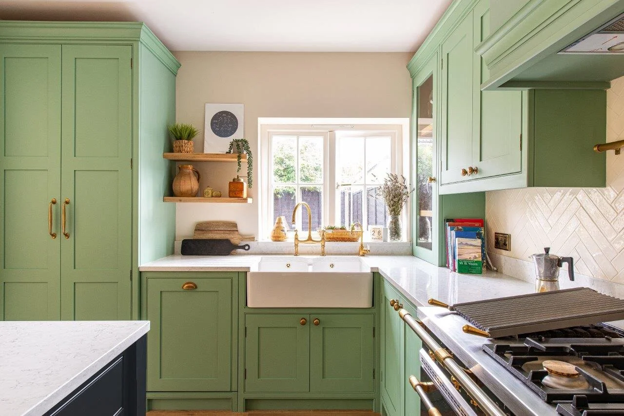 Green kitchen with white quartz worktops, double Belfast sink and brass tap in front of window