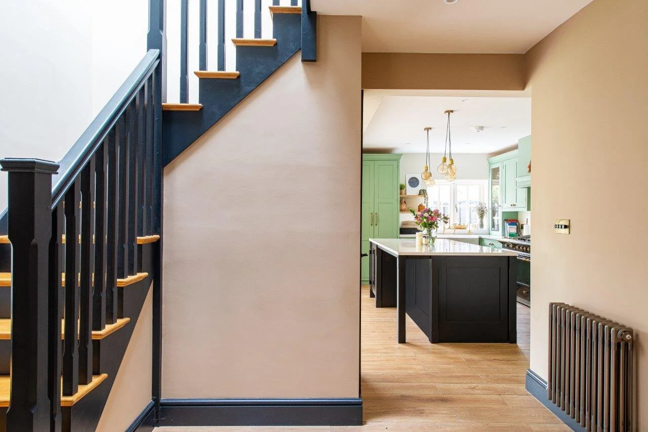 Mint green kitchen with large black kitchen island, white quartz worktops and industrial brass pendant lights above.