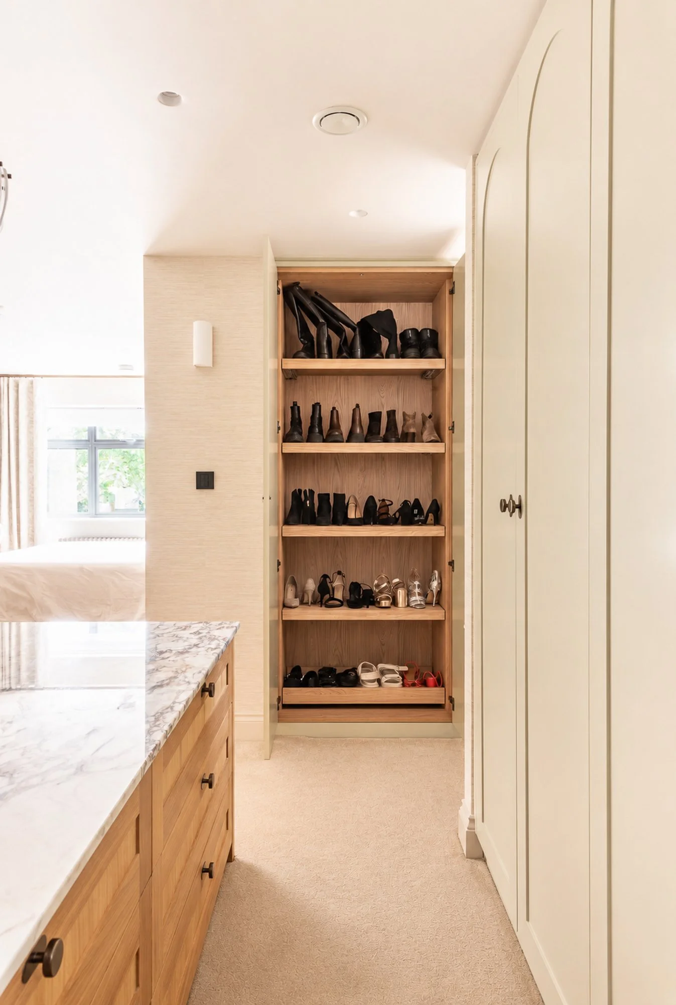 A wooden shoe rack filled with various types of shoes, with a kitchen counter and cabinetry nearby in a well-lit home interior.