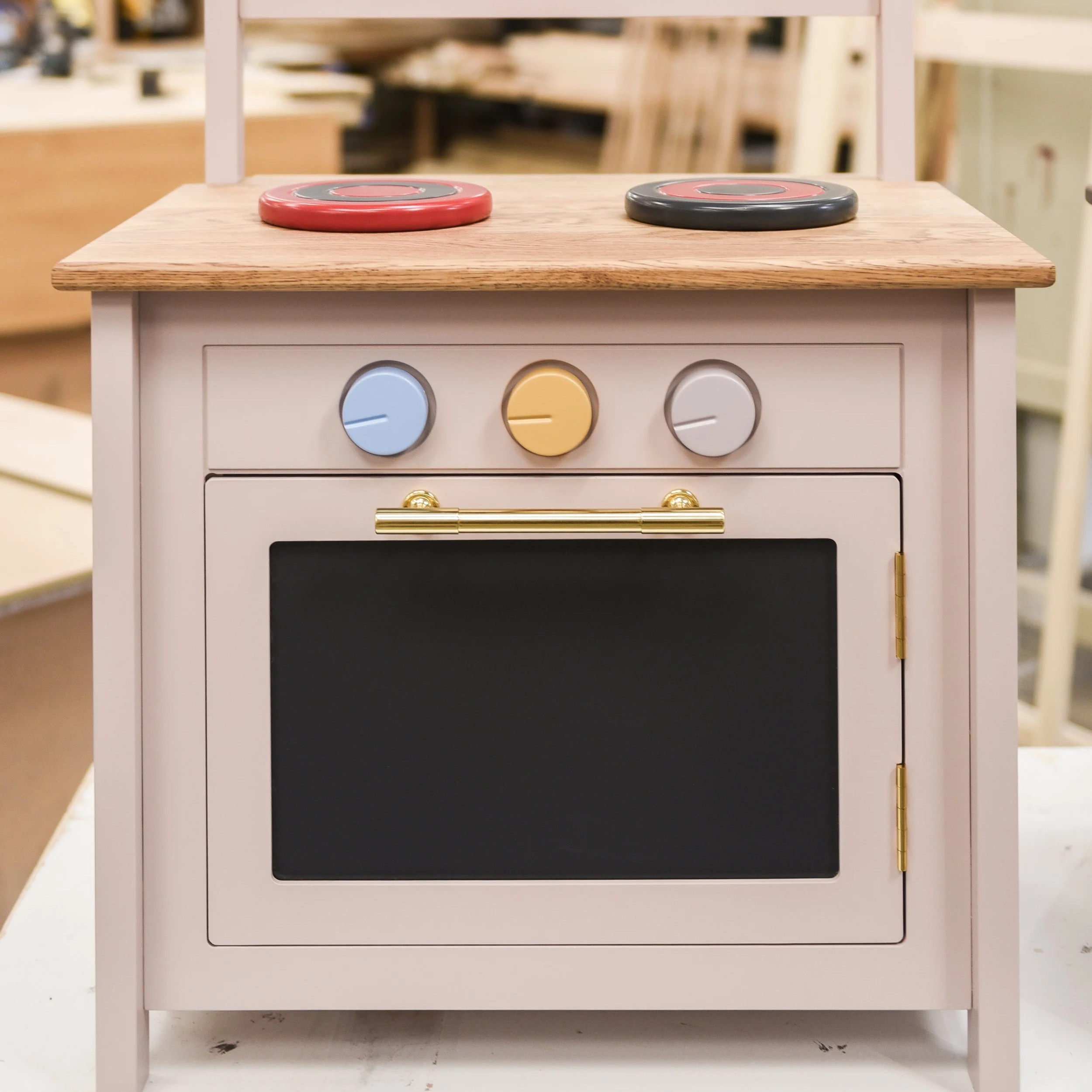 Toy kitchen stove with two black and red burners on a light wood countertop, white base, and pastel-colored control knobs.