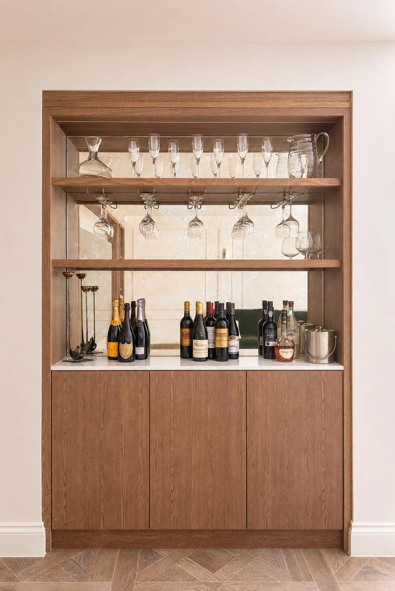 Wooden bar cabinet with wine bottles, hanging glasses, and decorative glassware on the shelves.