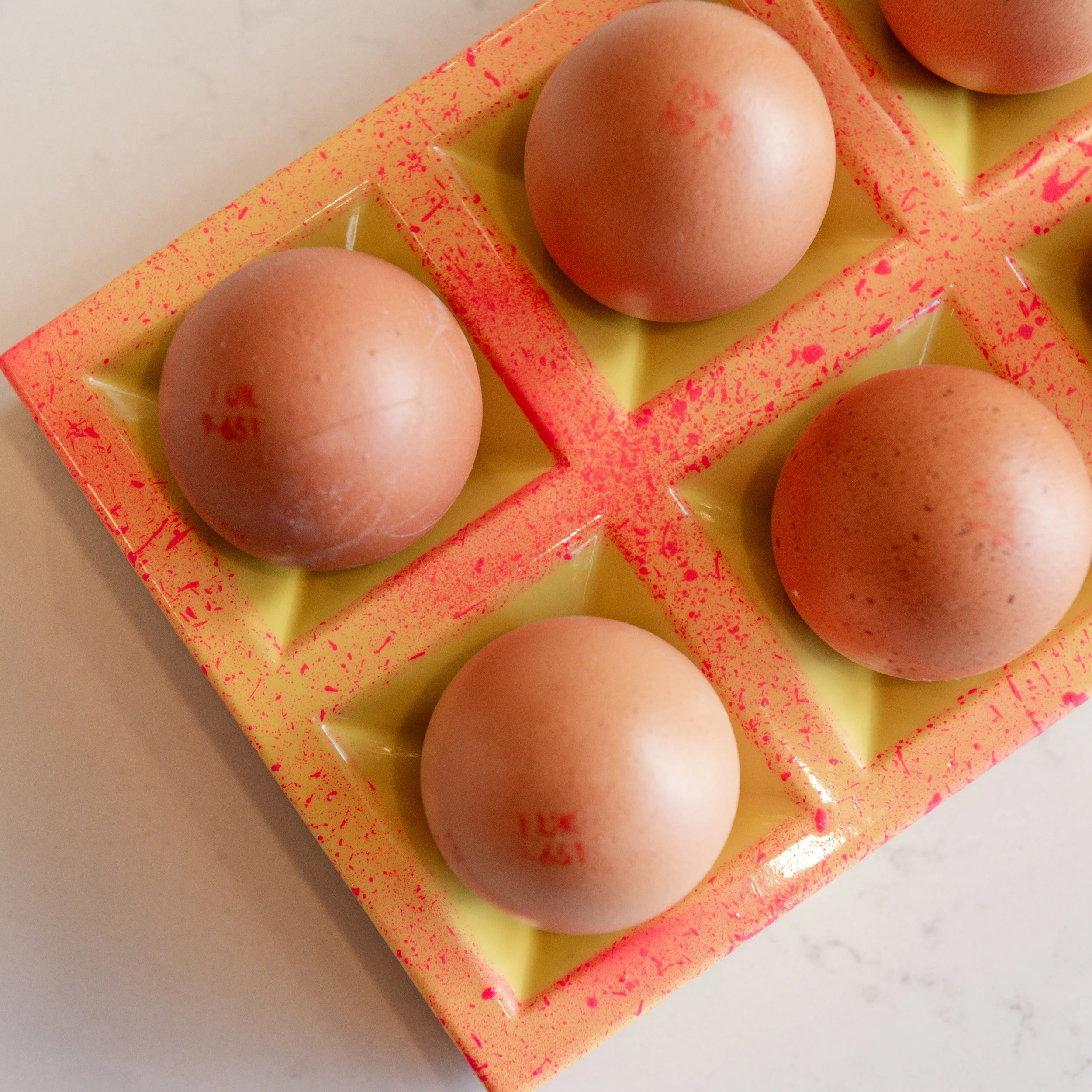 A close-up of a yellow plastic egg carton with a pink speckled pattern, holding brown eggs.