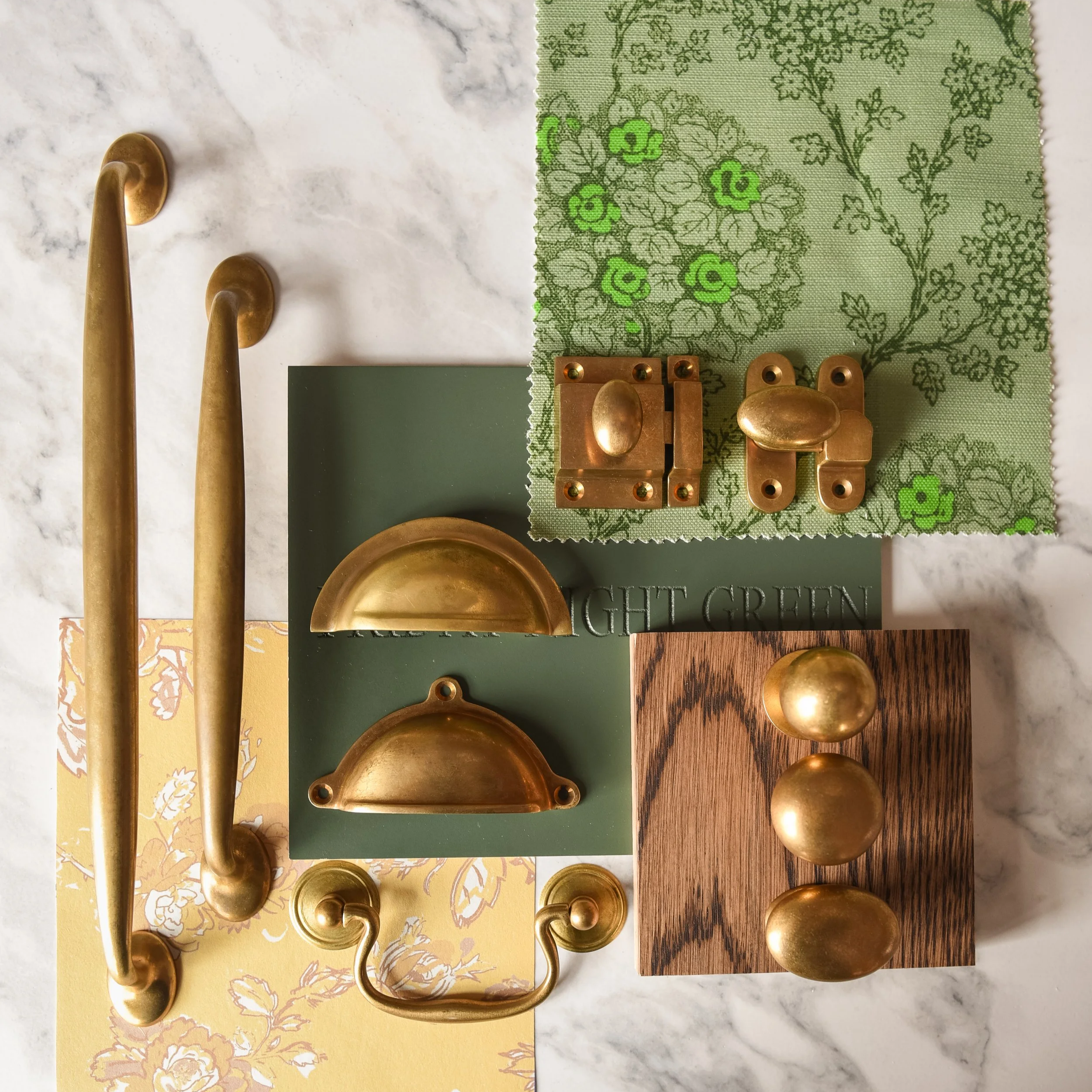 An assortment of gold-colored metal hardware pieces arranged on a marble and patterned paper background. The hardware includes hooks, hinges, and knobs of various shapes and sizes, all with a shiny finish.