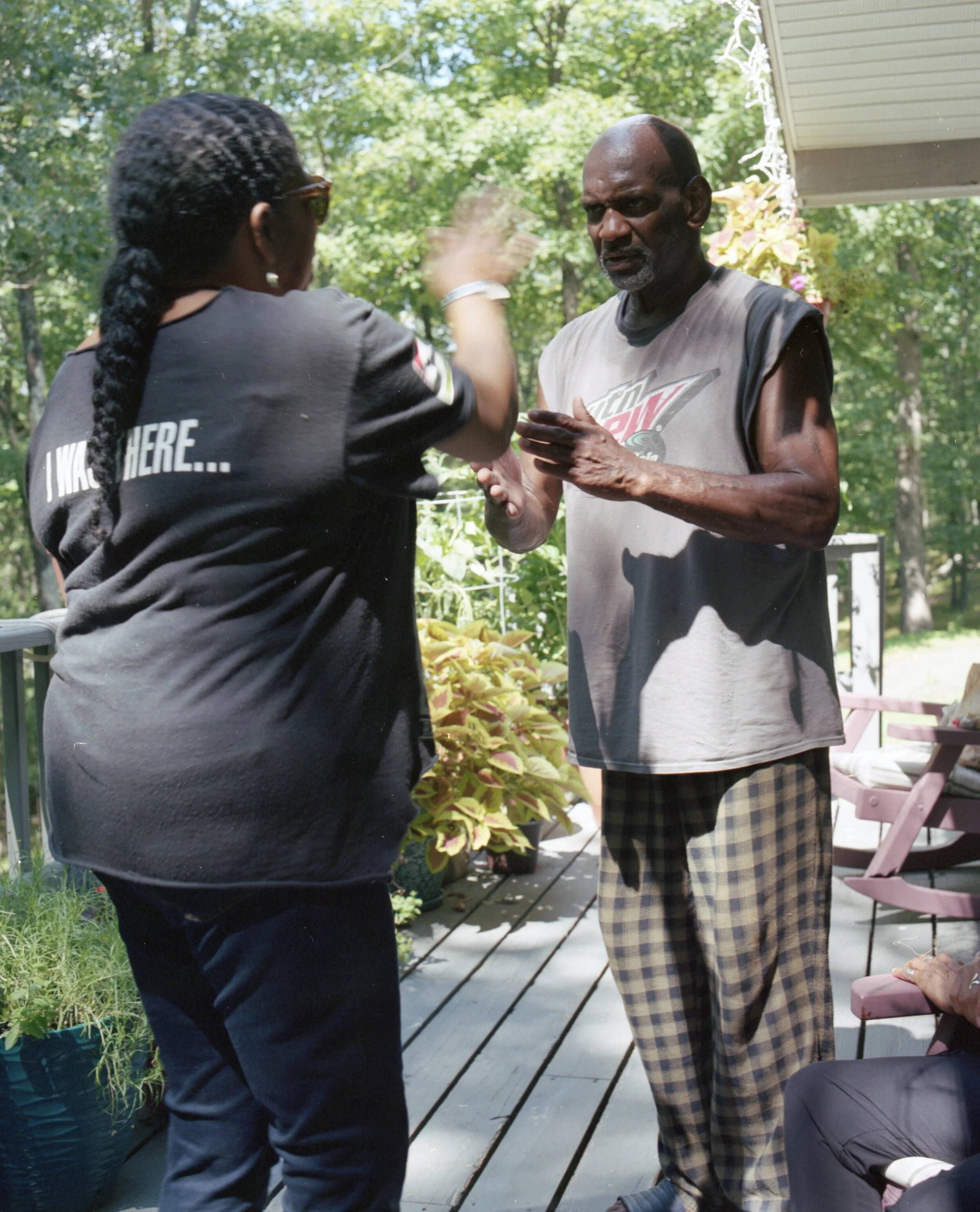 A woman is giving a high five to an older man on a wooden deck surrounded by lush green trees and plants in the daytime.