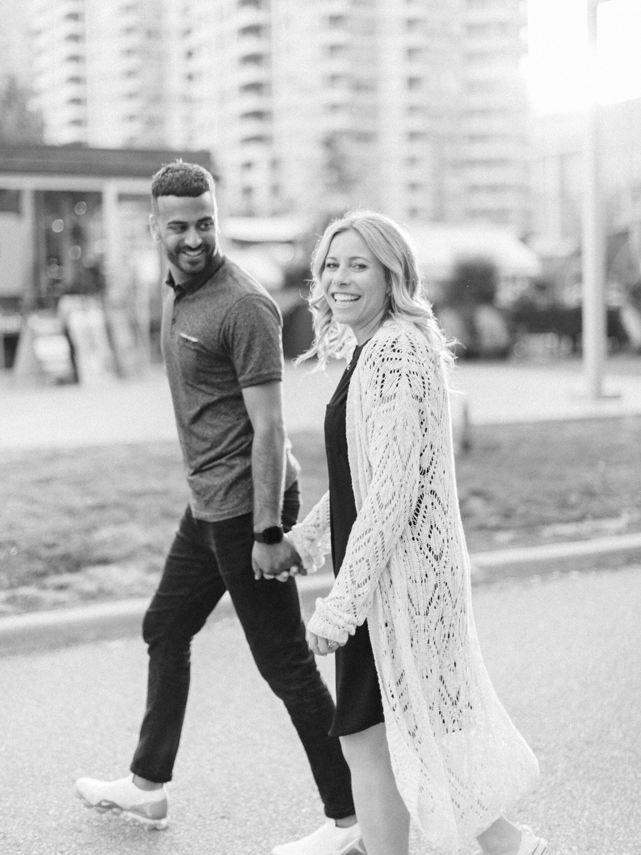 cute urban couple crossing the street and looking back for a candid photo during their downtown toronto engagement session at queens quay