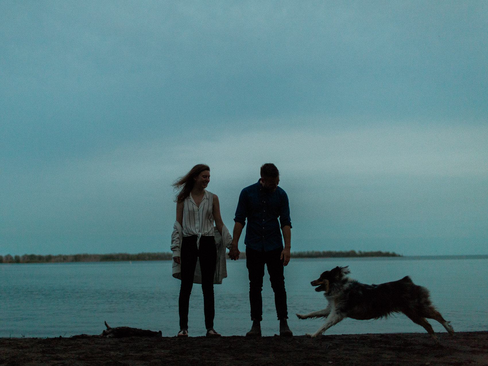 silhouette of engaged couple posing on the beach with their dog during a sunset engagement shoot