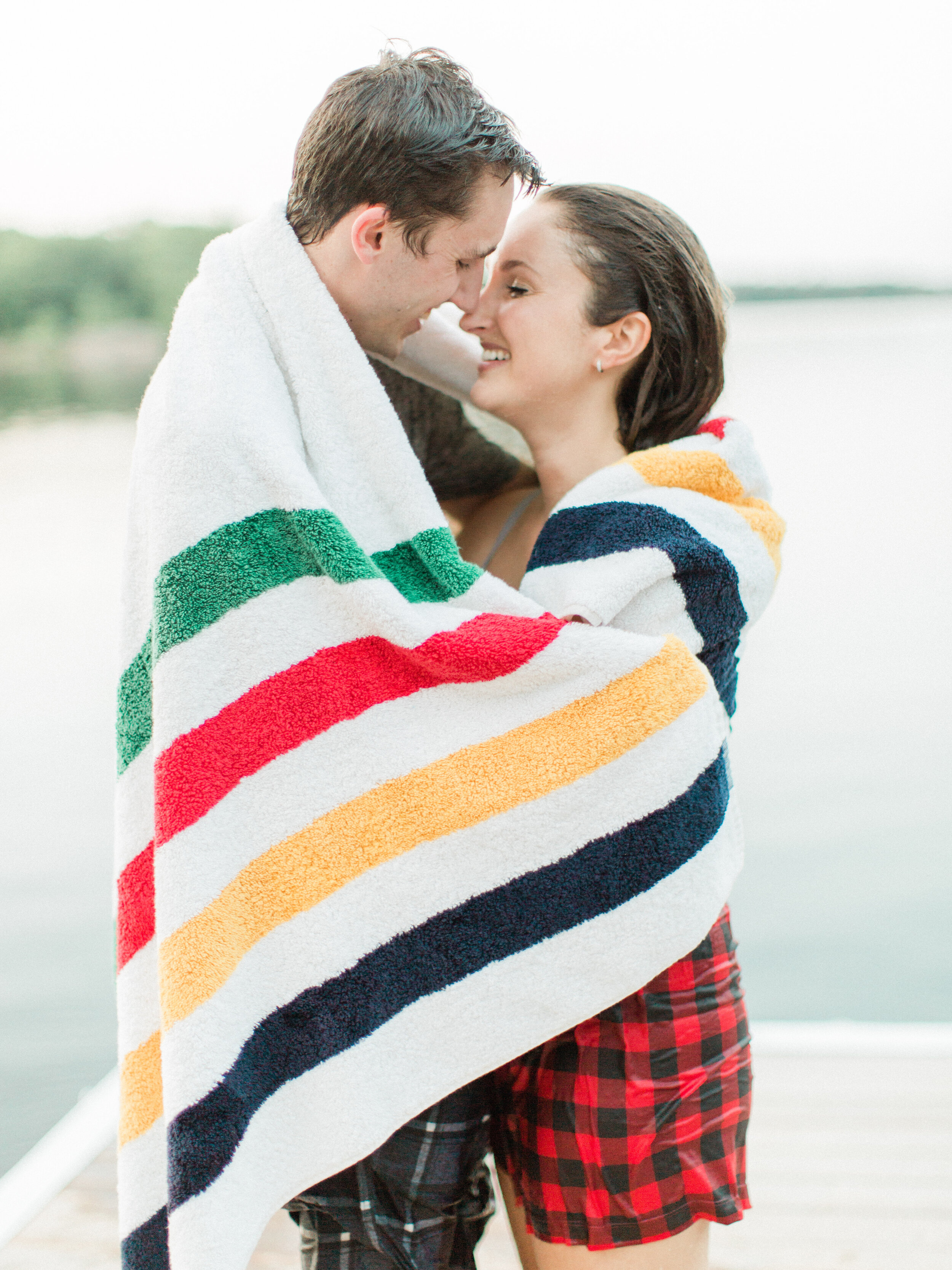 cute happy couple posing in hudsons bay blanket after jumping in the lake at their cottage engagement session in muskoka