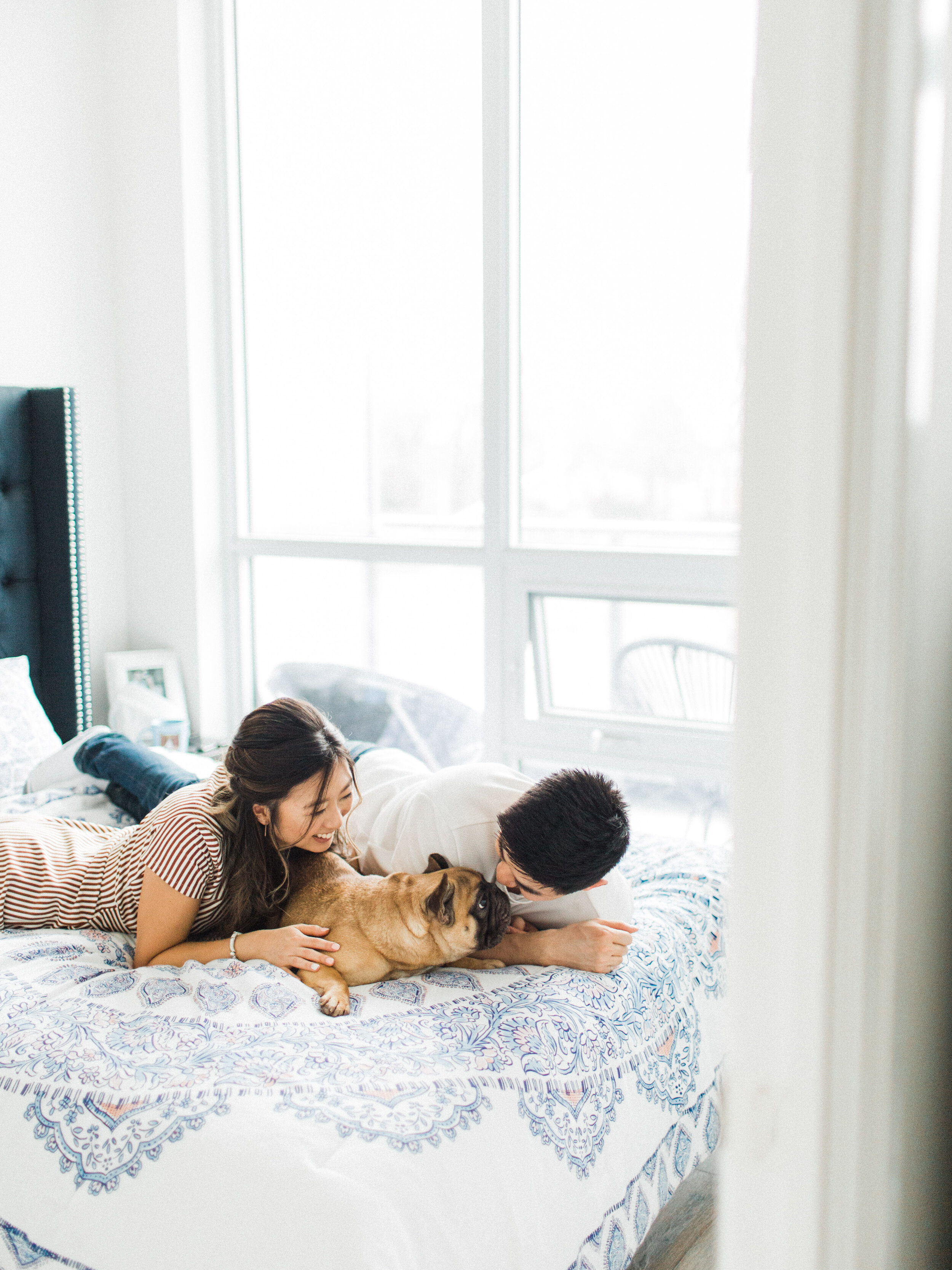 cute chinese couple snuggling with their dog on the bed at their at home engagement session