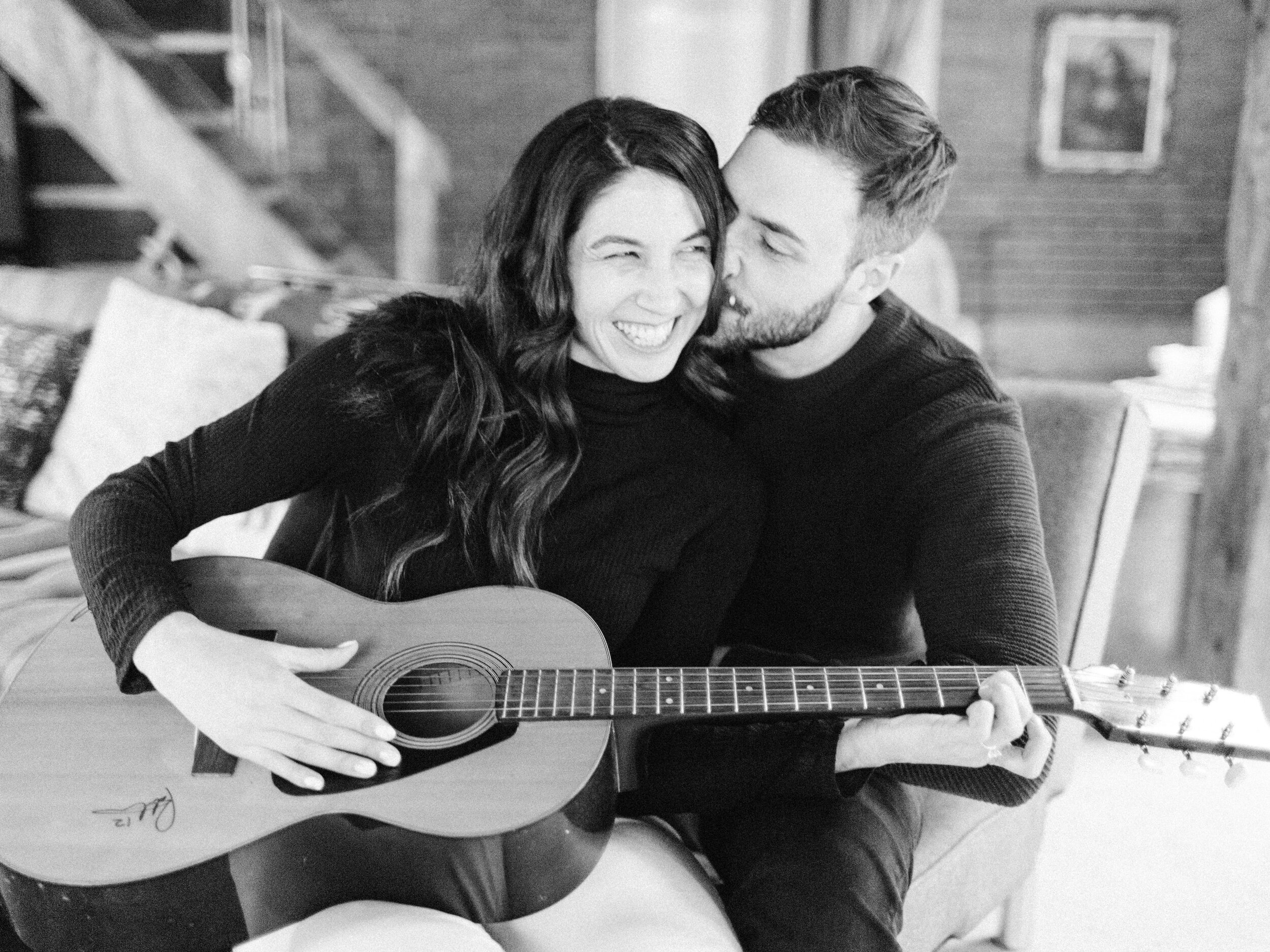 candid moment of a couple snuggling and playing the guitar at their at home engagement session in collingwood